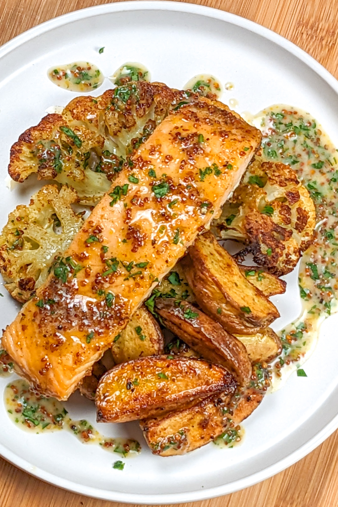 top view of Baked Cajun Honey Mustard Salmon Cauliflower Steaks & Potatoes with creamy honey Dijon mustard drizzled around it on a flat round plate