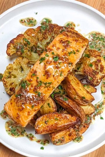 top view of Baked Cajun Honey Mustard Salmon Cauliflower Steaks & Potatoes with creamy honey Dijon mustard drizzled around it on a flat round plate