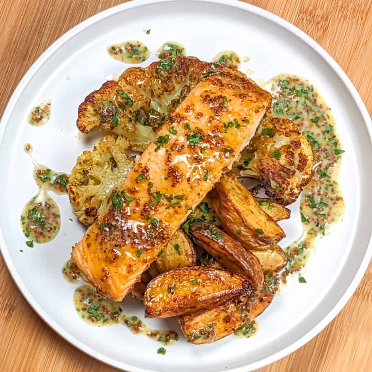 top view of Baked Cajun Honey Mustard Salmon Cauliflower Steaks & Potatoes with creamy honey Dijon mustard drizzled around it on a flat round plate