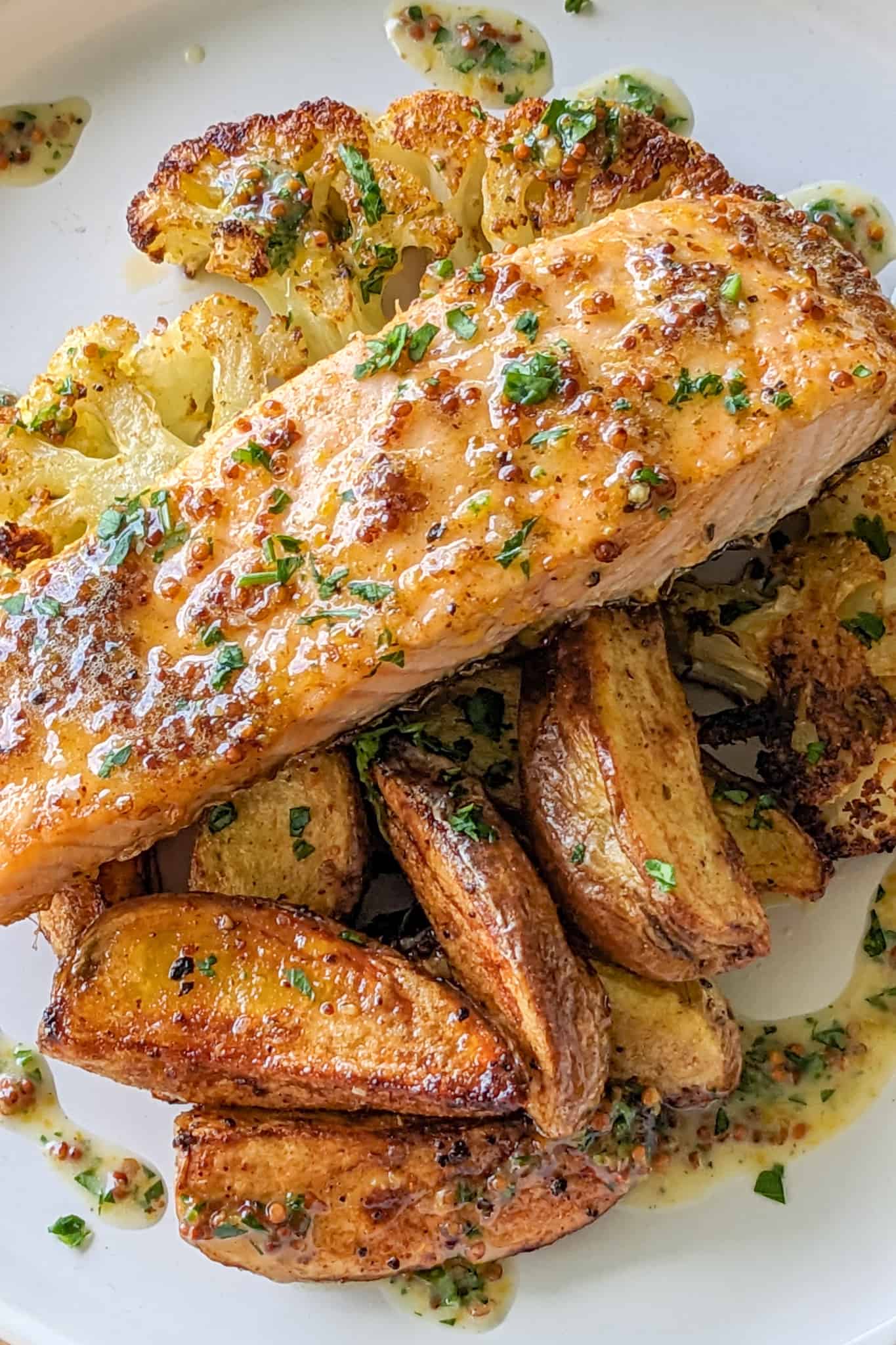 top view of Baked Cajun Honey Mustard Salmon Cauliflower Steaks & Potatoes with creamy honey Dijon mustard drizzled around it on a flat round plate