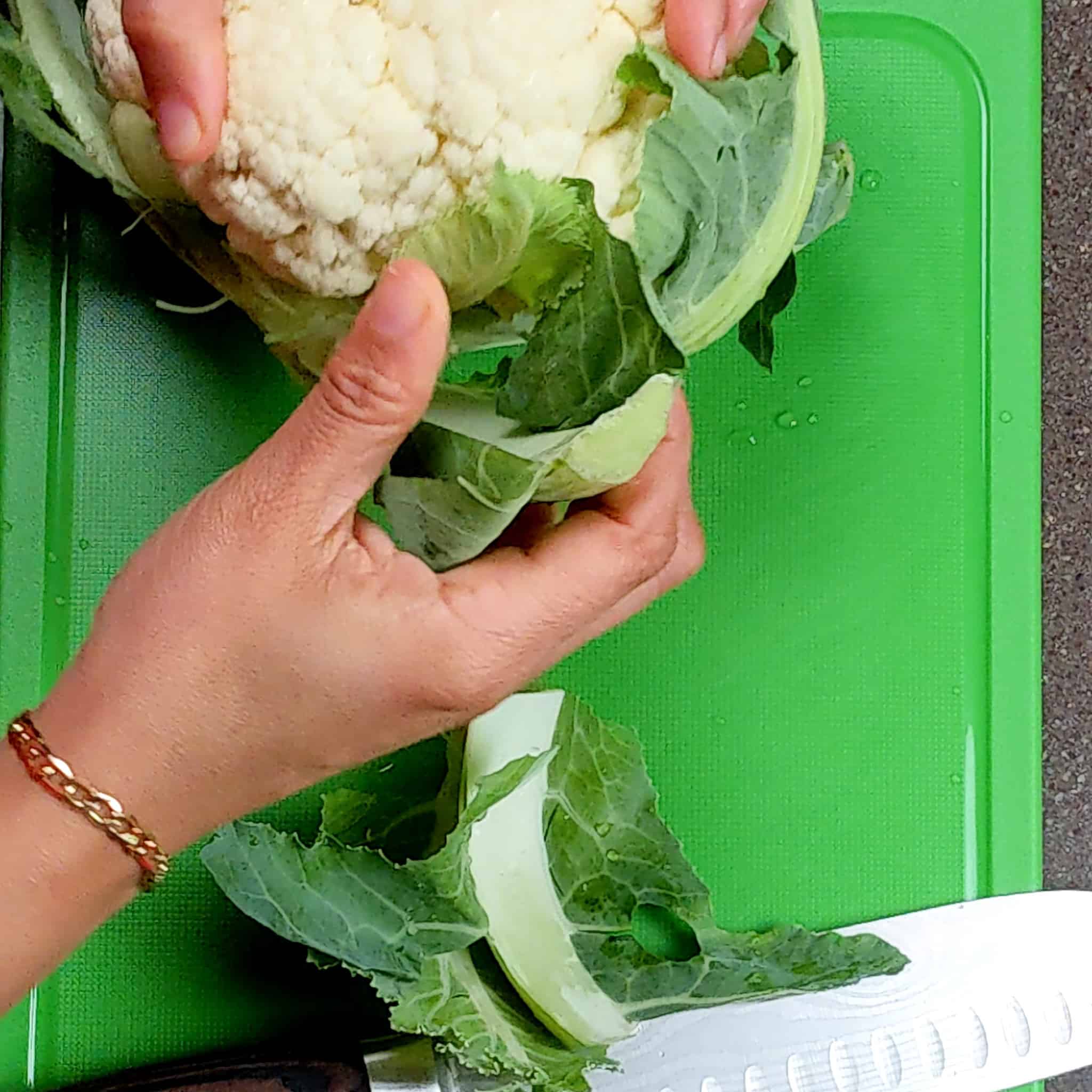 had picking off the leaves of the cauliflower head on a cutting board