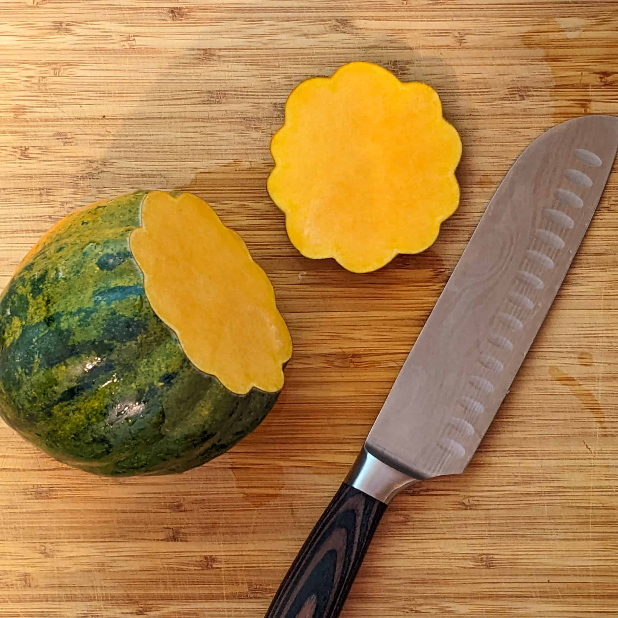 tip of the acorn squash sliced off  with both resting on the cutting board next to a santoku knife
