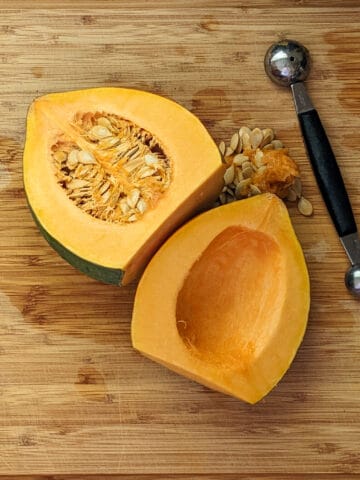 halved acorn squash with one seeded out facing up on a cutting board next to a two-sided melon baller