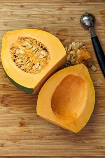 halved acorn squash with one seeded out facing up on a cutting board next to a two-sided melon baller