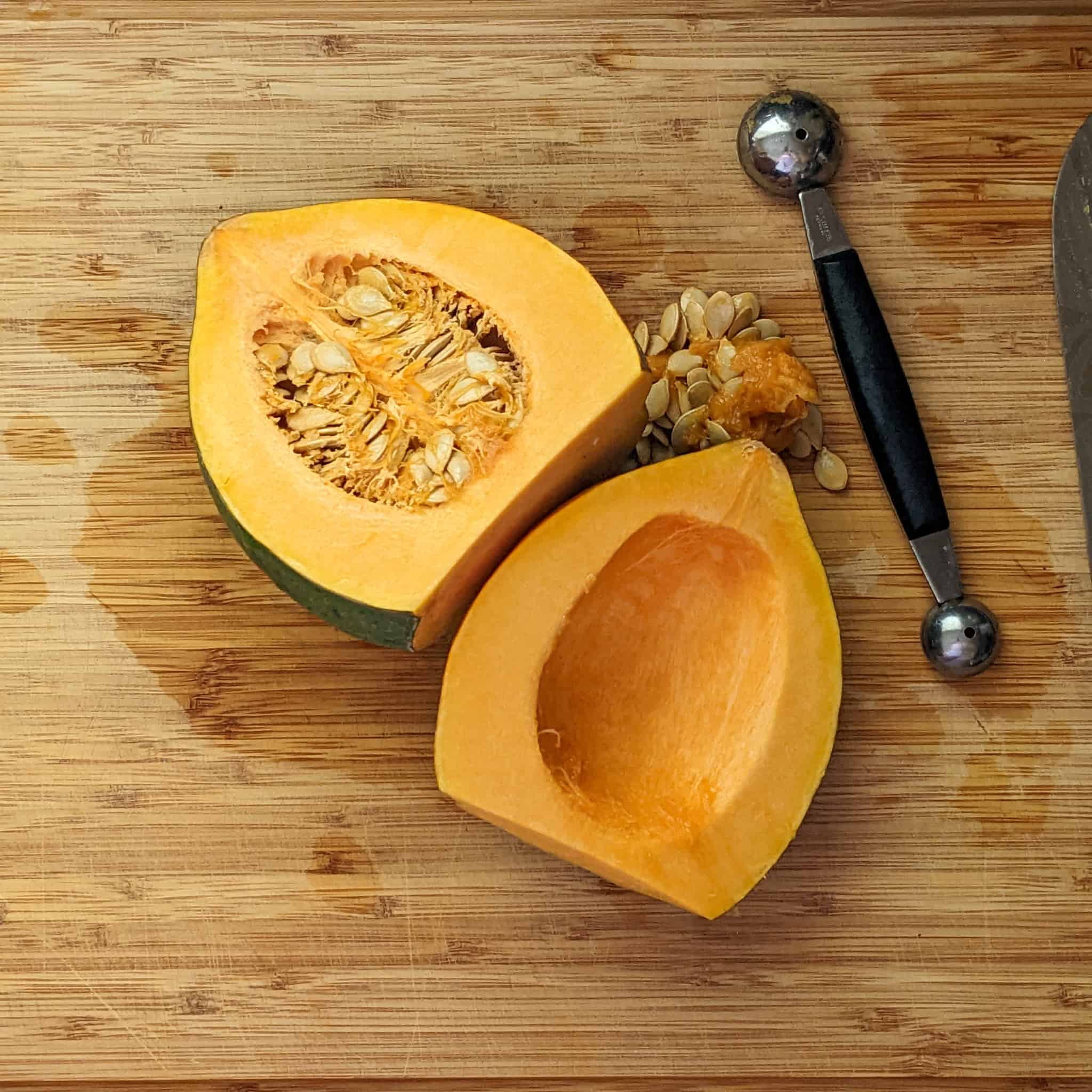 halved acorn squash with one seeded out facing up on a cutting board next to a two-sided melon baller