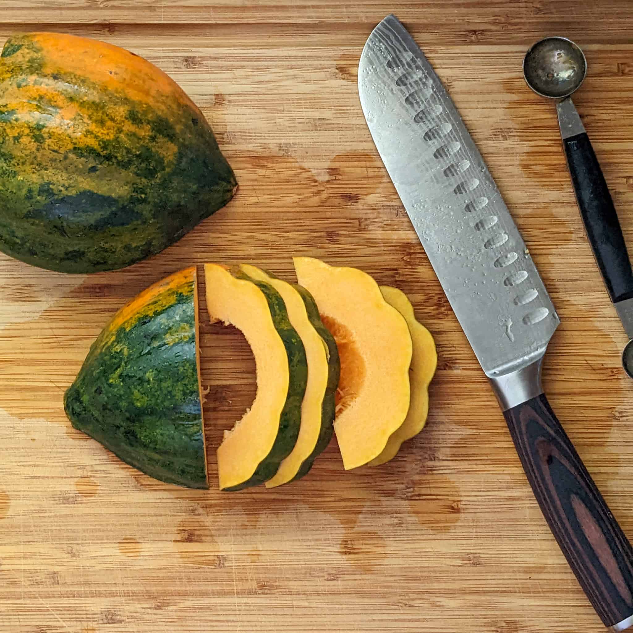 two halved acorn squash skin side up. one in whole while the other has been cut into sliced rings half way through laying on a cutting board next to a knife