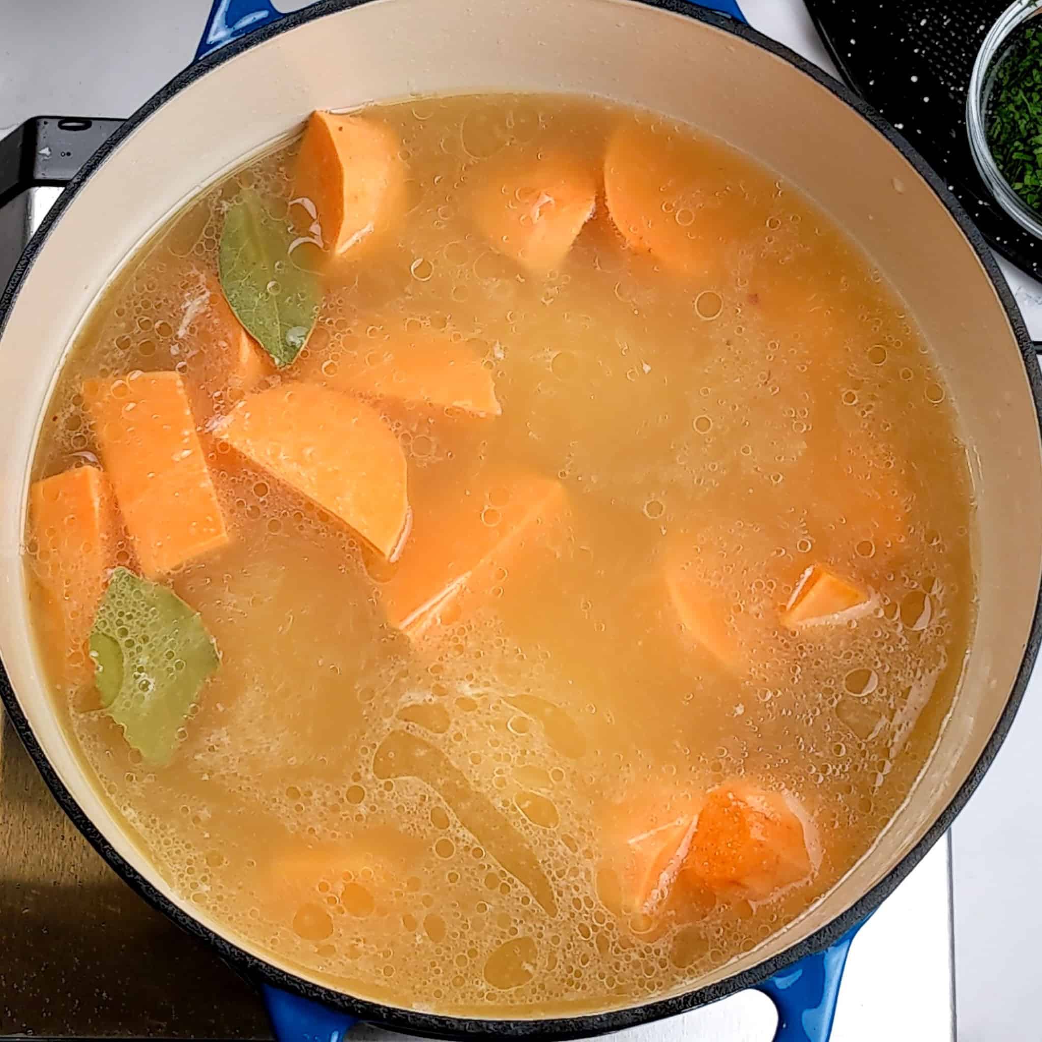 chicken broth with sweet potato chunks and bay leaves in a dutch oven