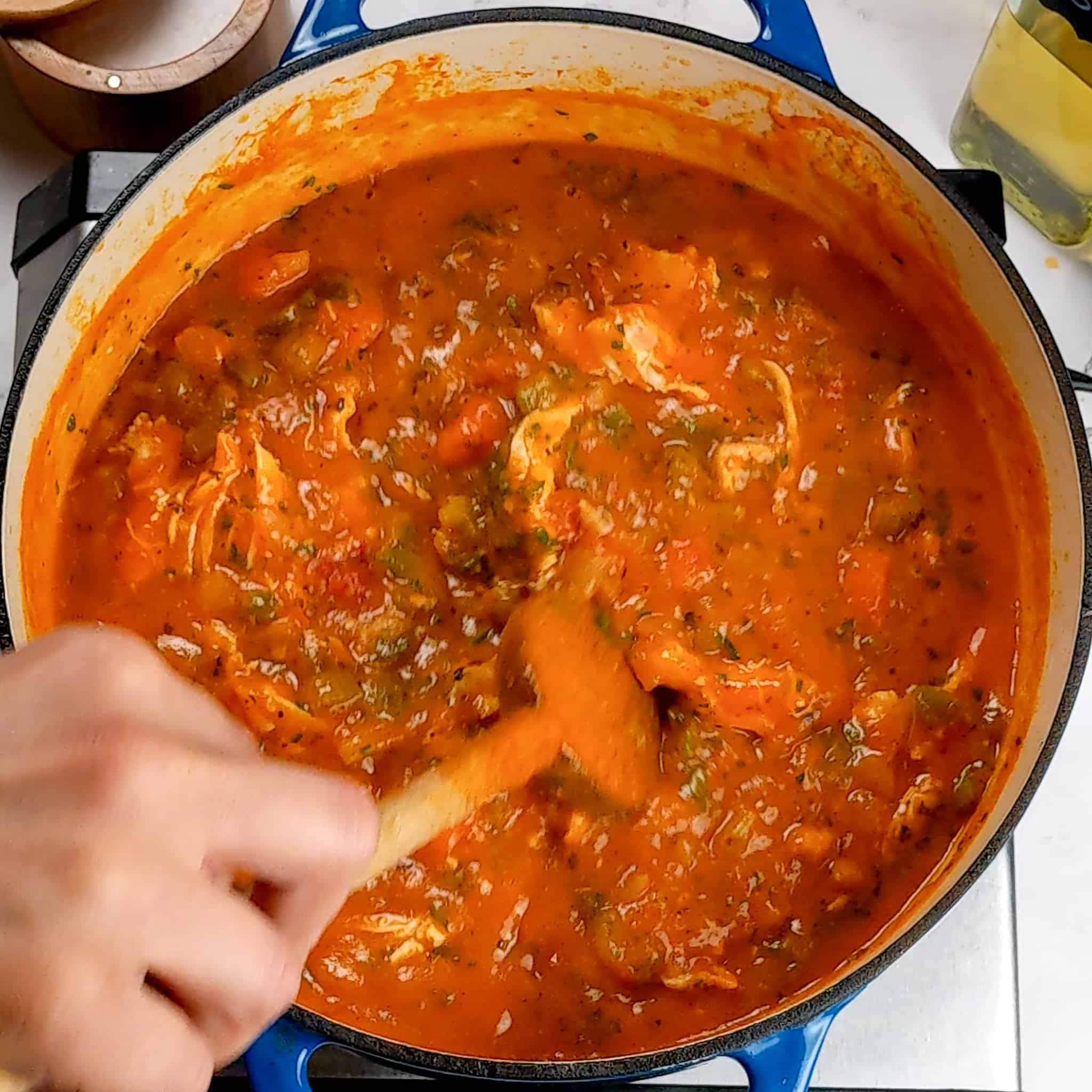 sweet potato chicken soup being stirred in a dutch oven with a wooden spoon