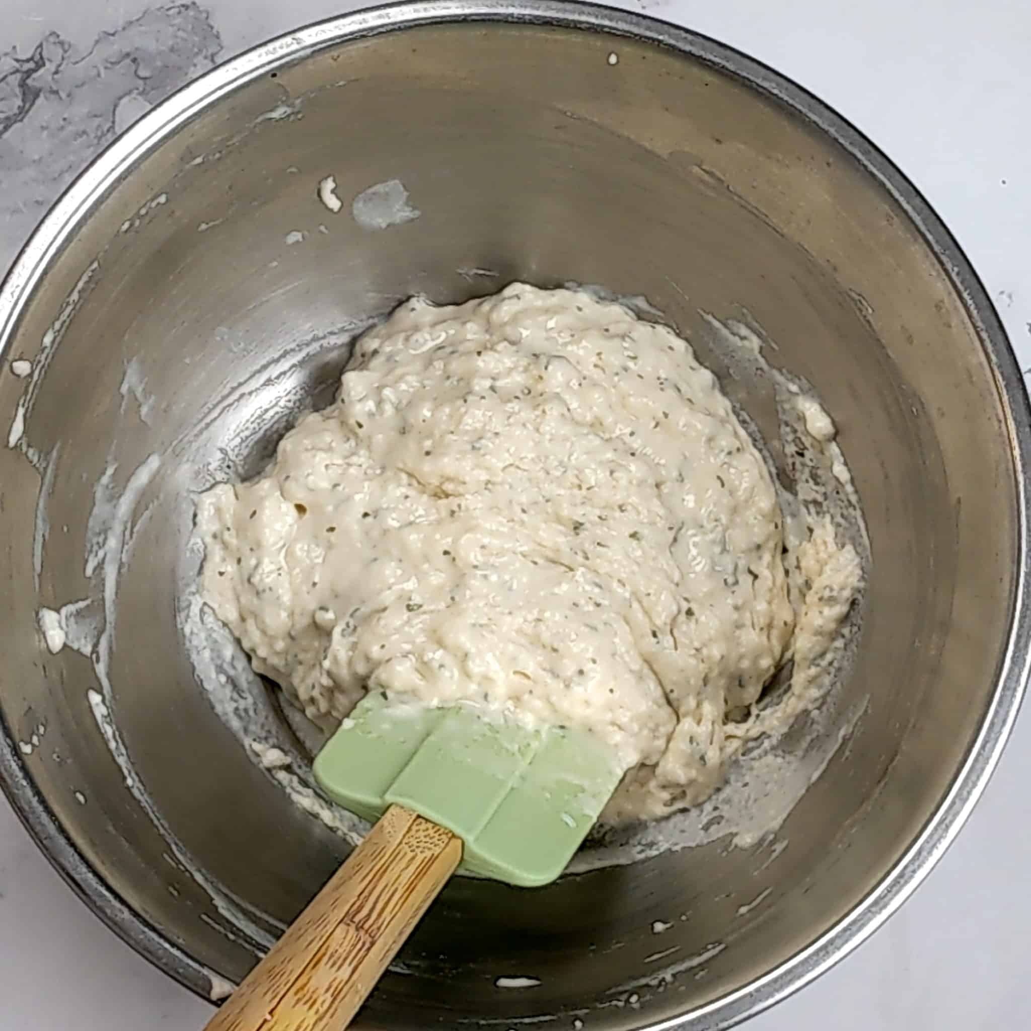 dumpling dough batter resting in a stainless steel mixing bowl with a silicon spatula with a wooden handle