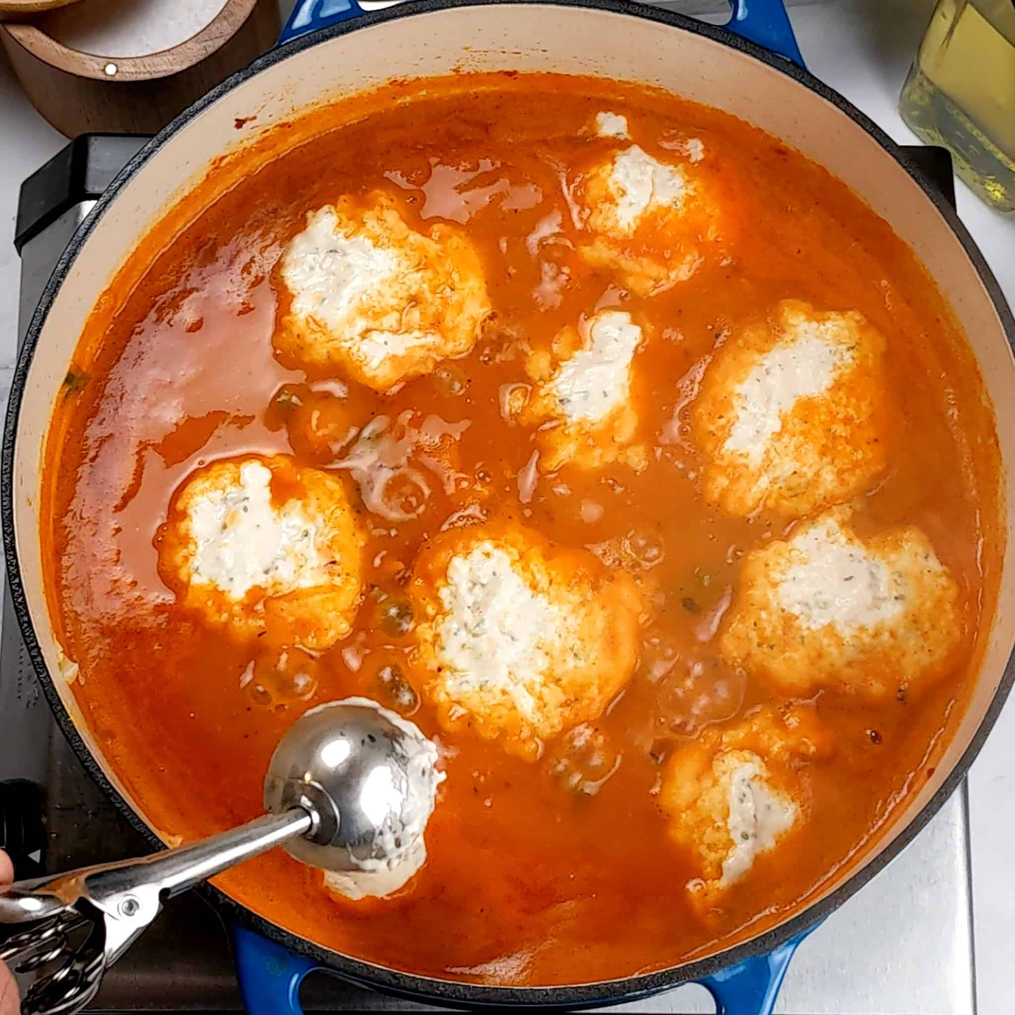 dumpling dough being dropped in the sweet potato chicken soup with a small scooper