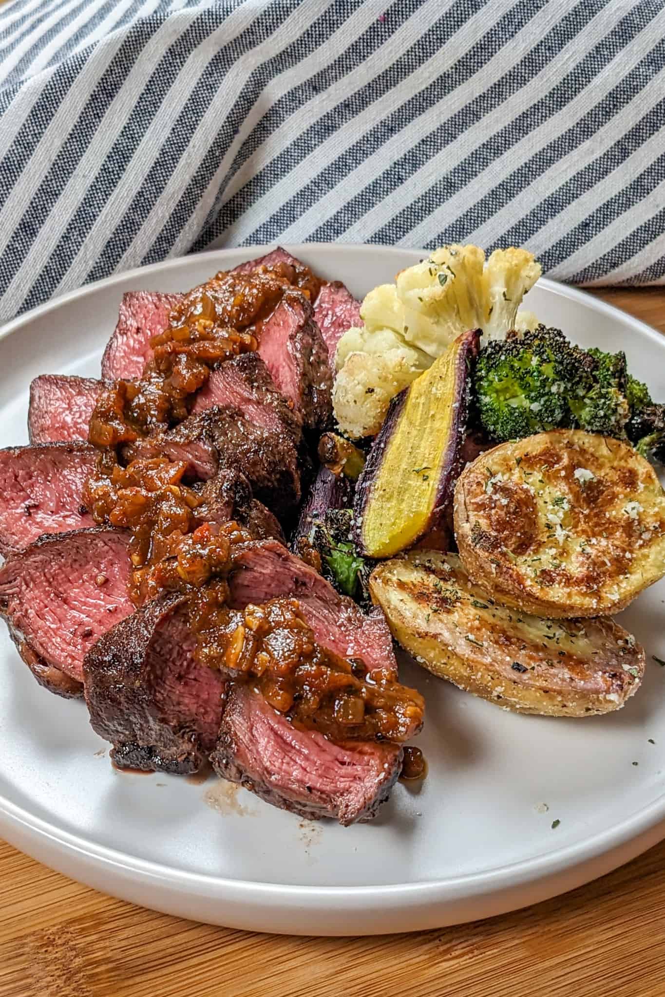 side view of the Pan-Seared Sirloin Steak with Spicy Baharat Sauce dish on a round flat plate