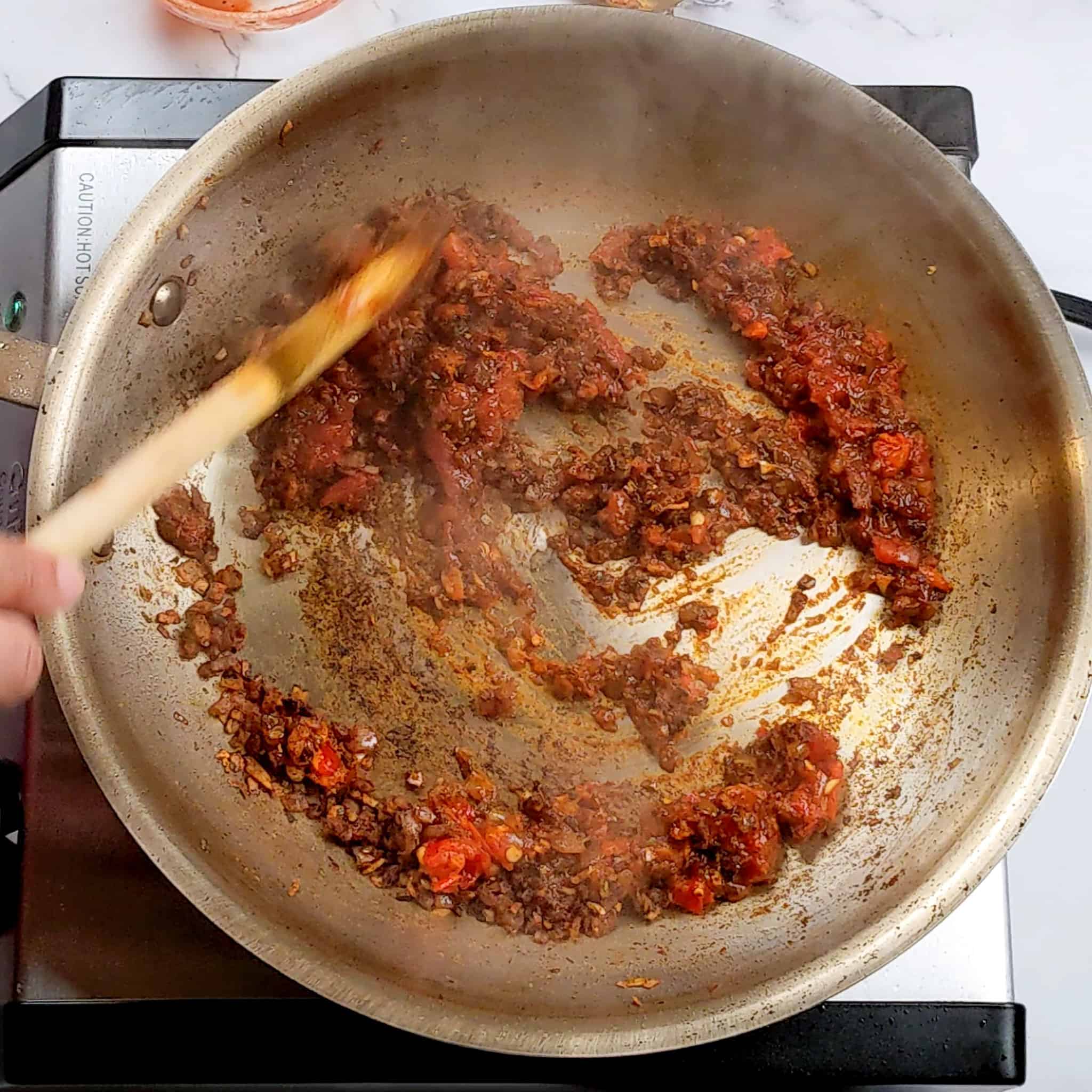 a thick paste being stirred with a wooden spoon in a stainless steel frying pan.