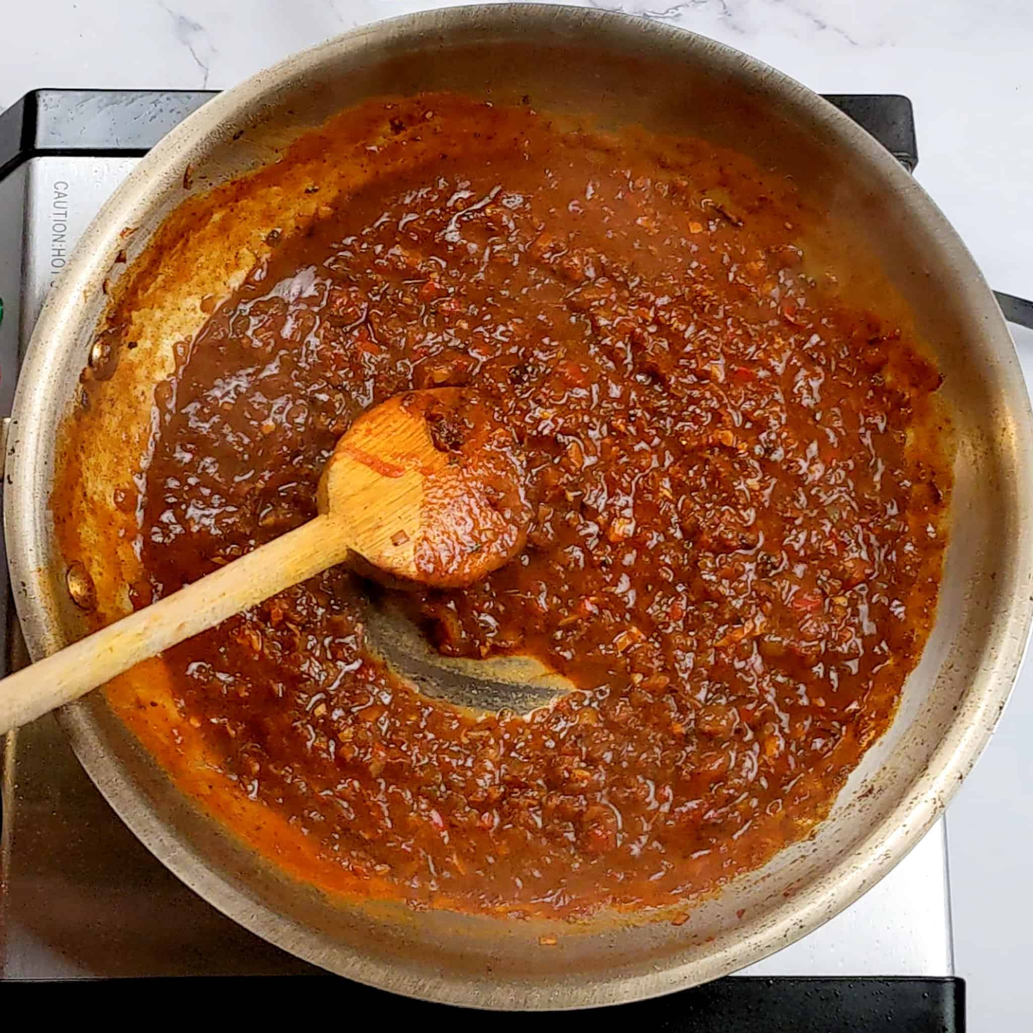 a thick chunky sauce in a all-clad stainless steel frying pan with a wooden spoon