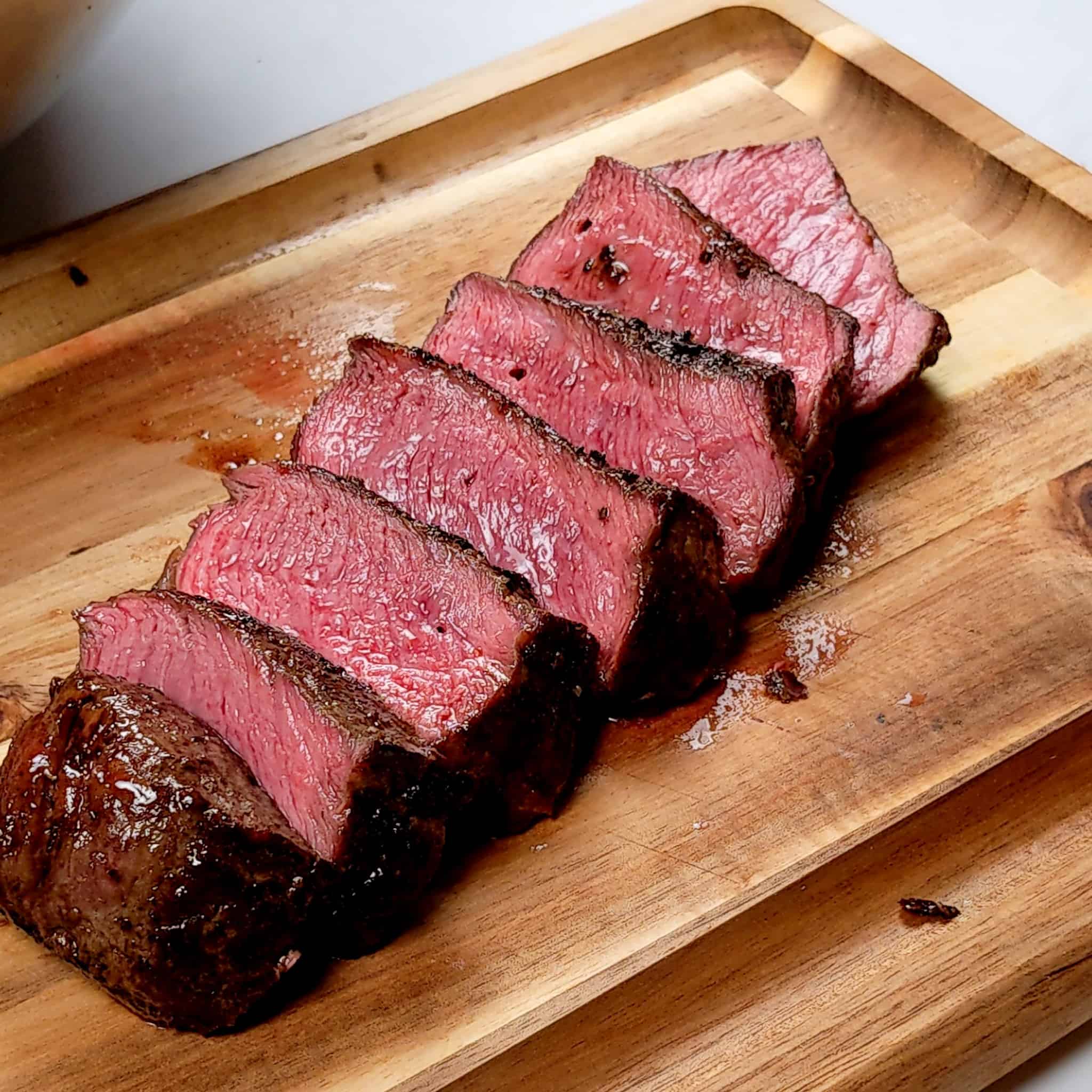 medium rear sliced top sirloin steak cascading on a small wooden cutting board