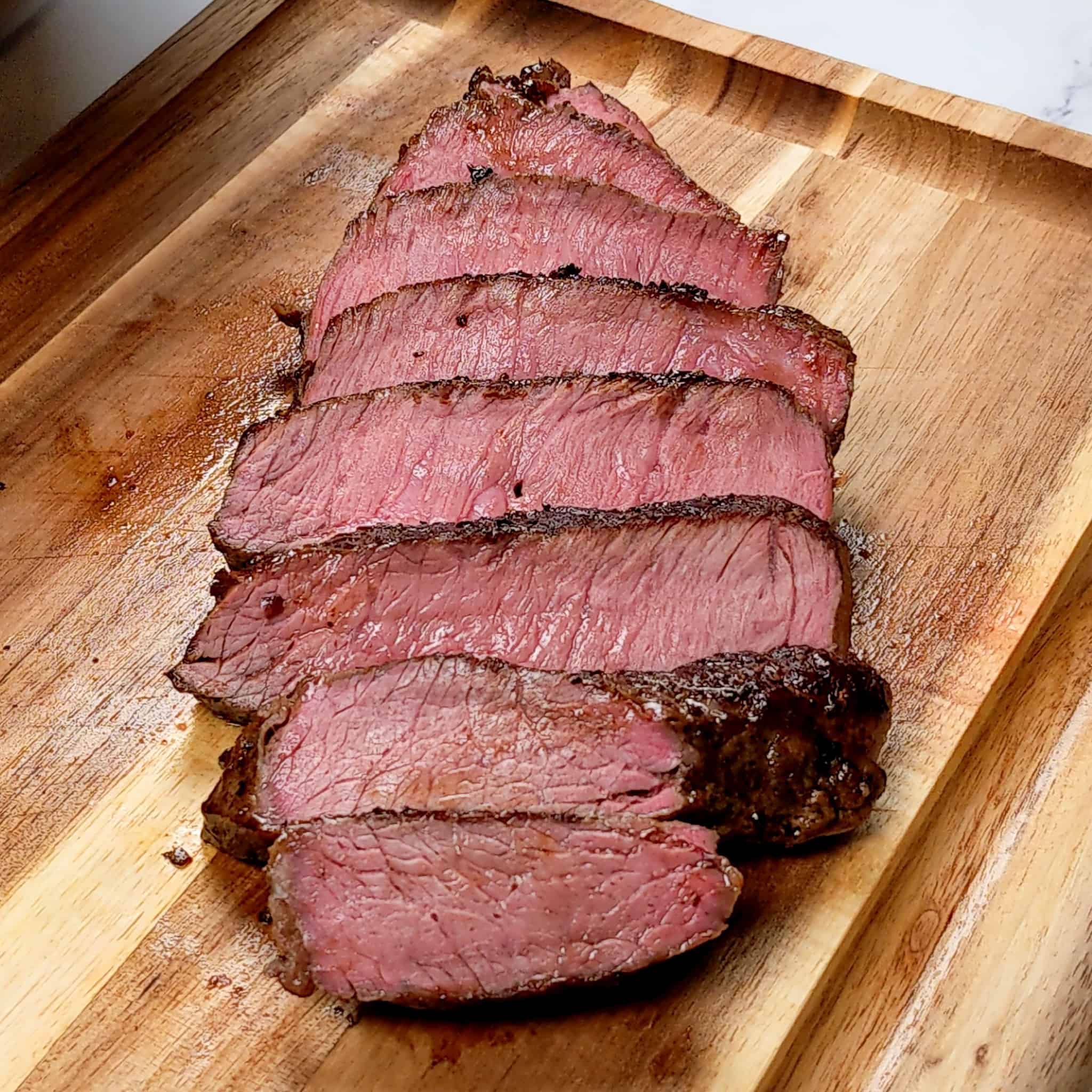 medium sliced top sirloin steak cascading on a small wooden cutting board