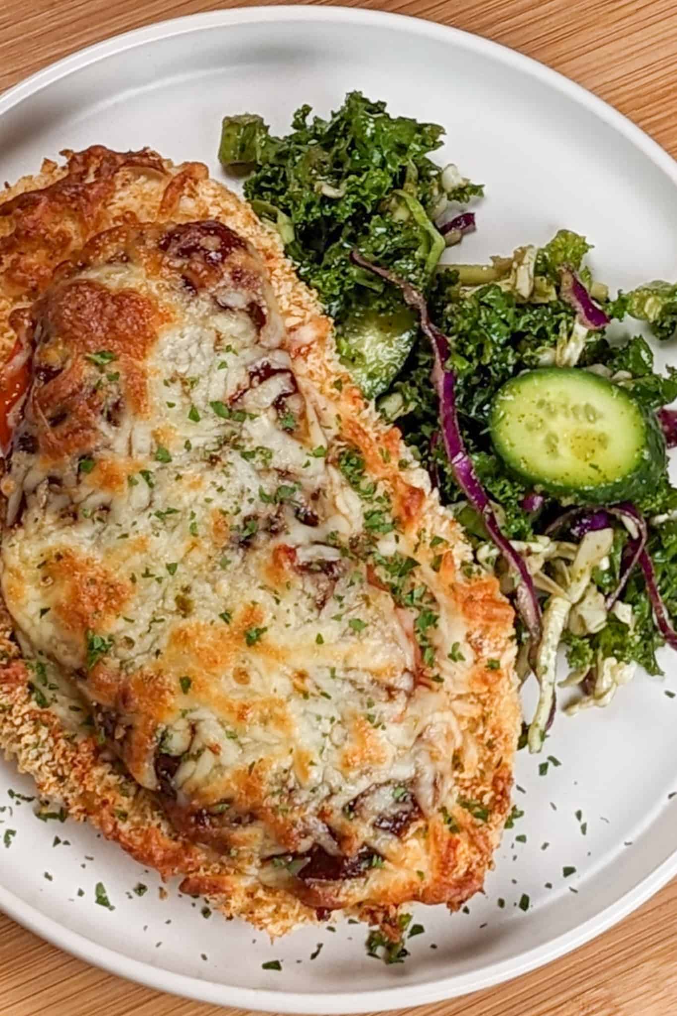 top view the Easy Baked Cheesy Crispy Barbeque Chicken Cutlet recipe with a side salad on a round plate.