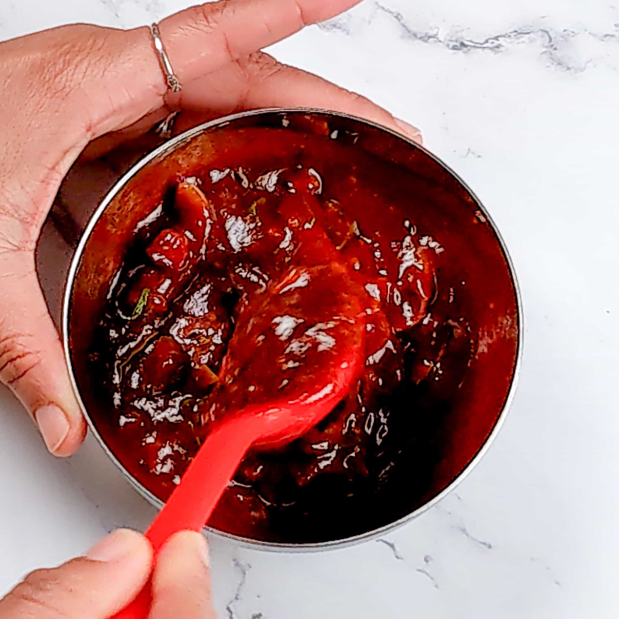 Barbeque sauce in a small stainless steel mixing bowl being mixed with a silicone spoon.