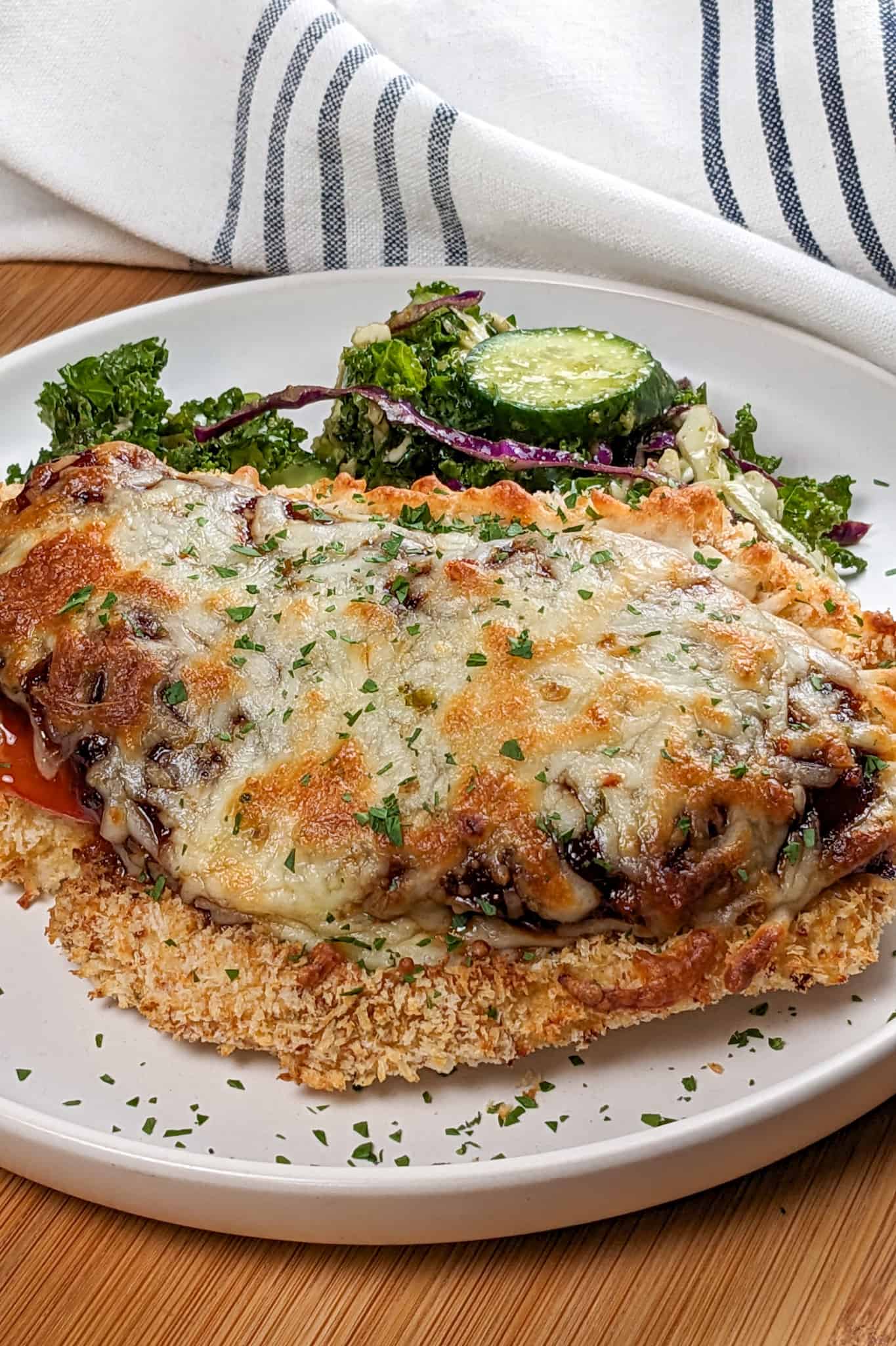 Side view the Easy Baked Cheesy Crispy Barbeque Chicken Cutlet recipe with a side salad on a round plate.