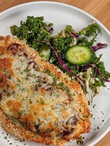 Side view the Easy Baked Cheesy Crispy Barbeque Chicken Cutlet recipe with a side salad on a round plate.