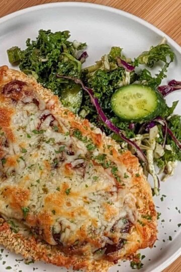 Side view the Easy Baked Cheesy Crispy Barbeque Chicken Cutlet recipe with a side salad on a round plate.