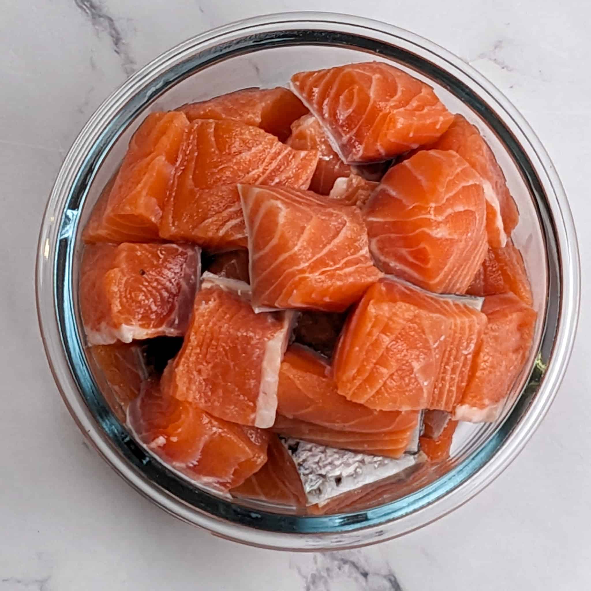 skin on salmon chunks in a glass round bowl.