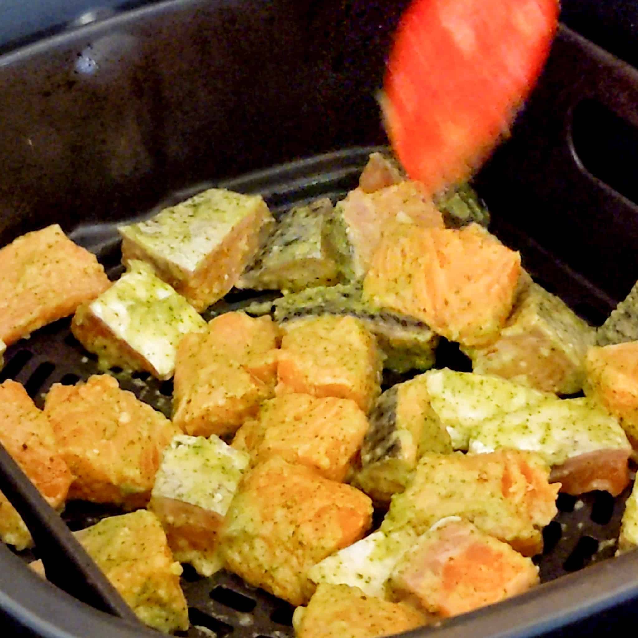 seasoned salmon chunks being placed in the air fryer for the Air Fryer Spicy Cilantro Lime Salmon Salad Rice Bowl recipe