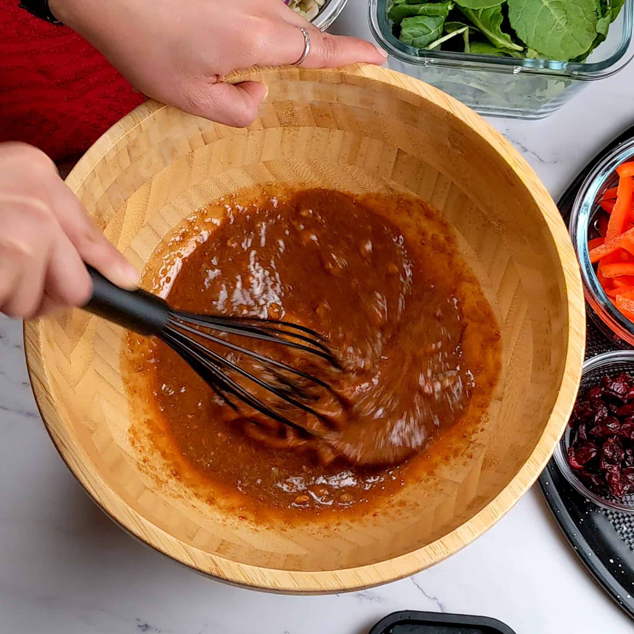 Wide wooden bowl with dressing being whisked with a silicone whisk