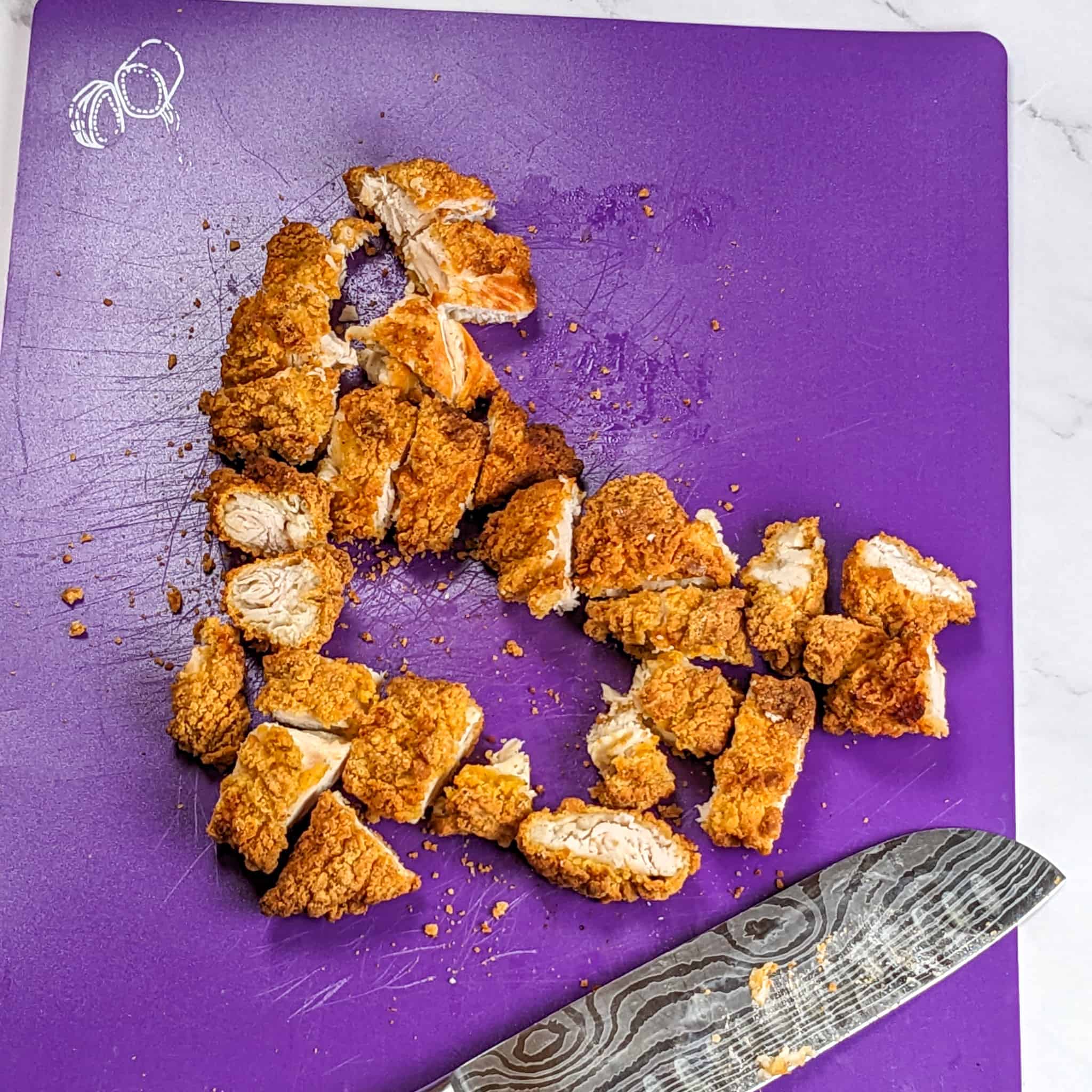 chopped chicken tenders on a cutting board for cooked meats next to a knife