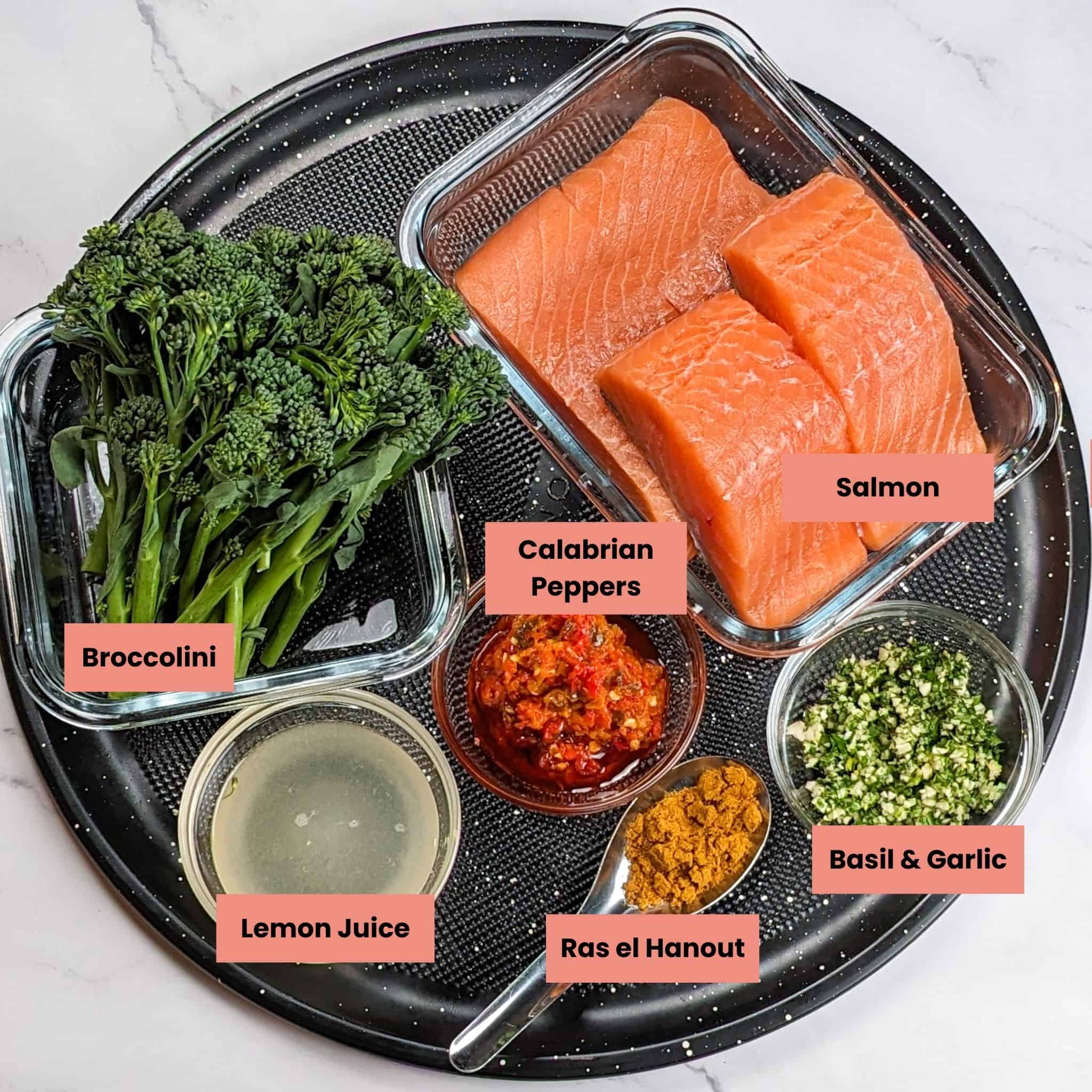 ingredients for the Calabrian Pepper Basil Baked Salmon and Broccolini in containers on a large round pizza pan.