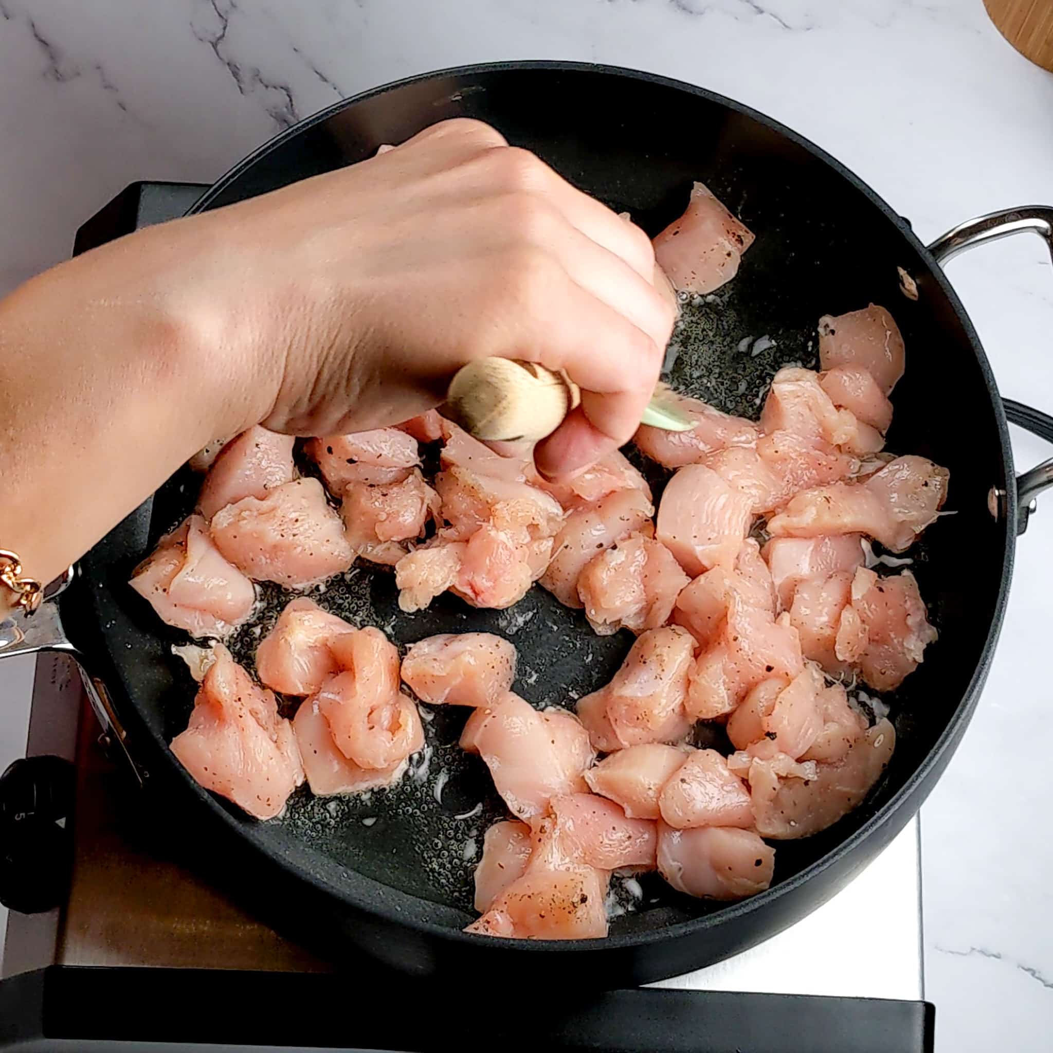 cubed chicken being separated with a silicone wooden handle spatula in a large nonstick saute pan