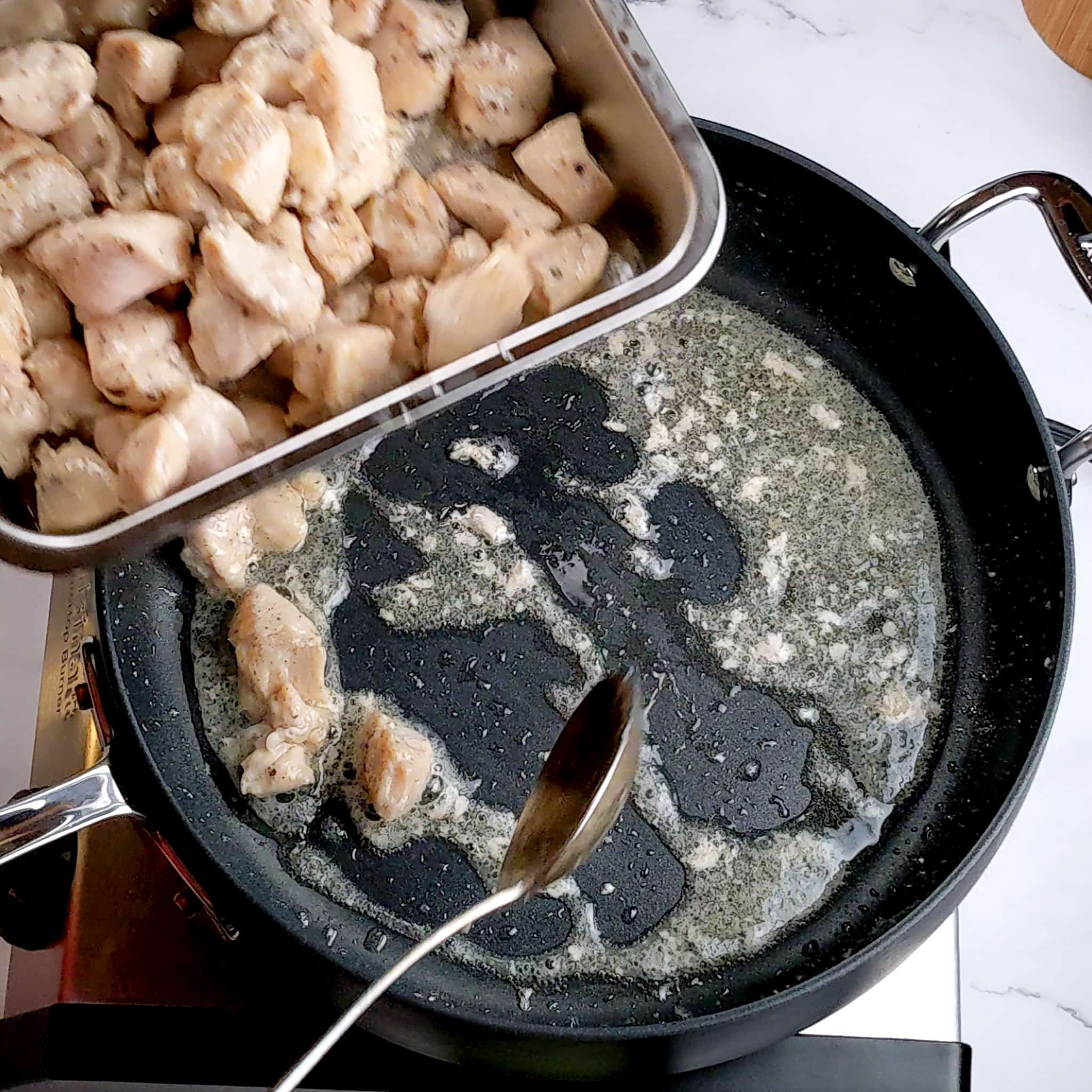 cooked chicken chunks being removed from the large saute pan