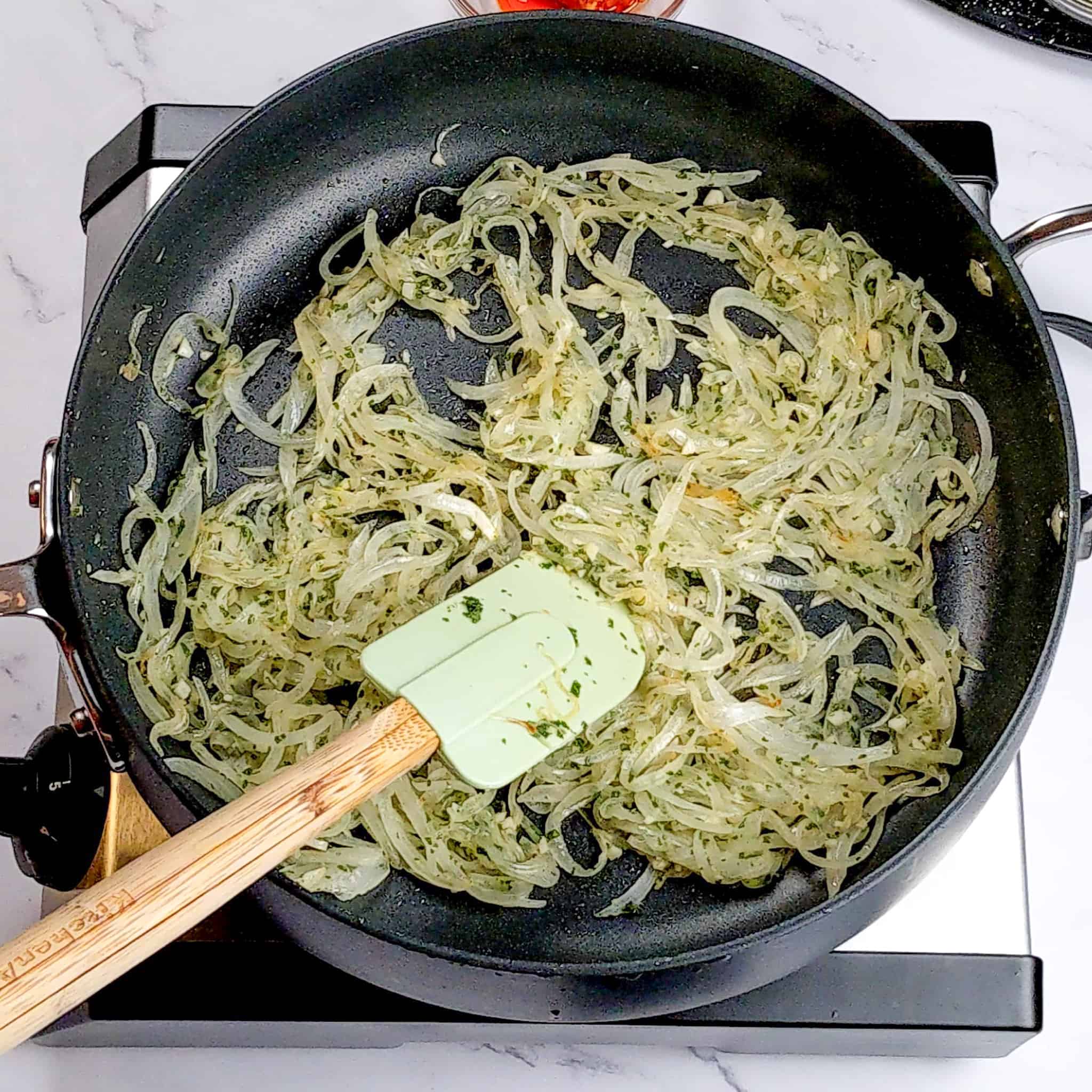 herbed thinly sliced onions being sauteed in a large saute pan with a silicone spatula for the sage pumpkin chicken pasta recipe.