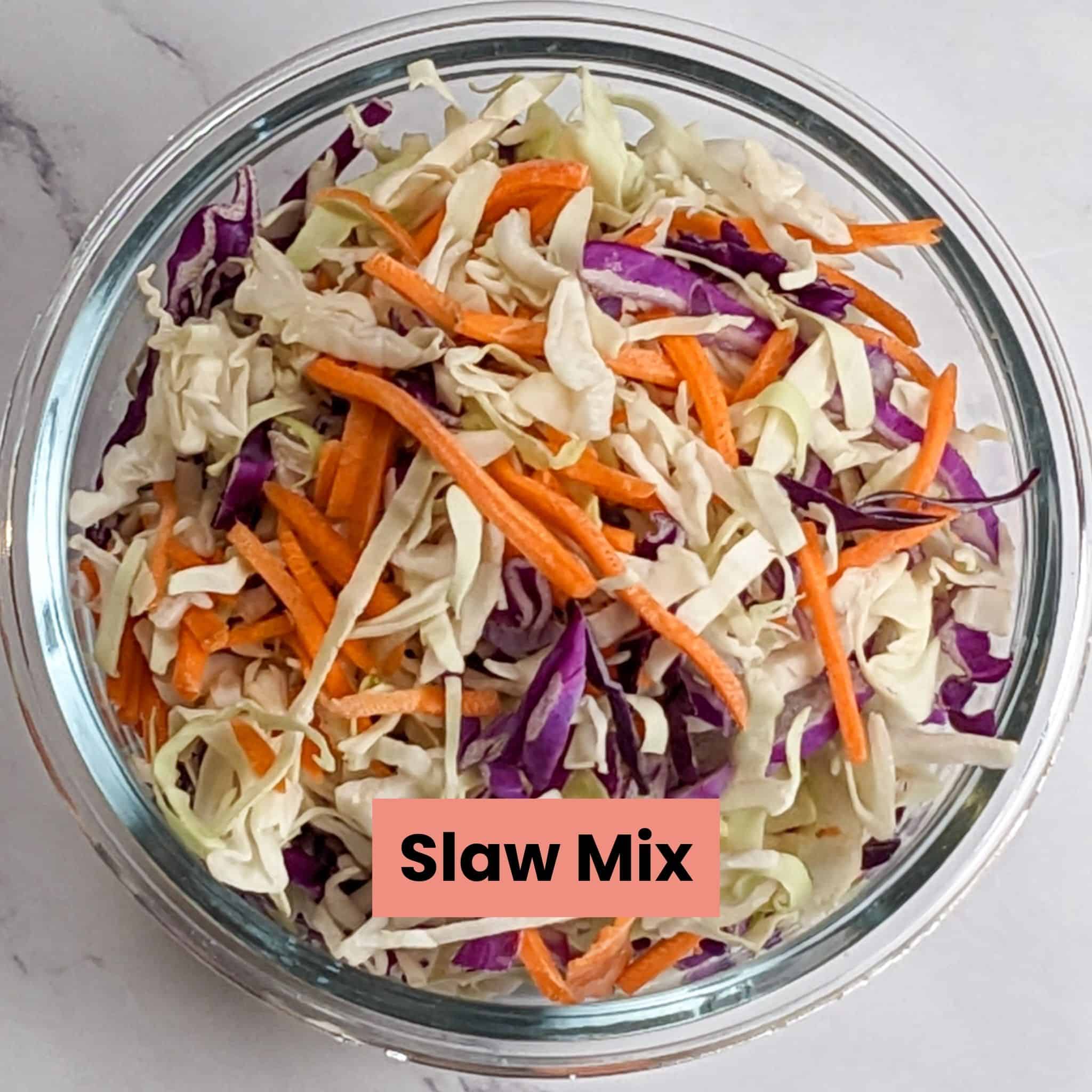 shredded cabbage and carrots making up the slaw in a deep round glass container