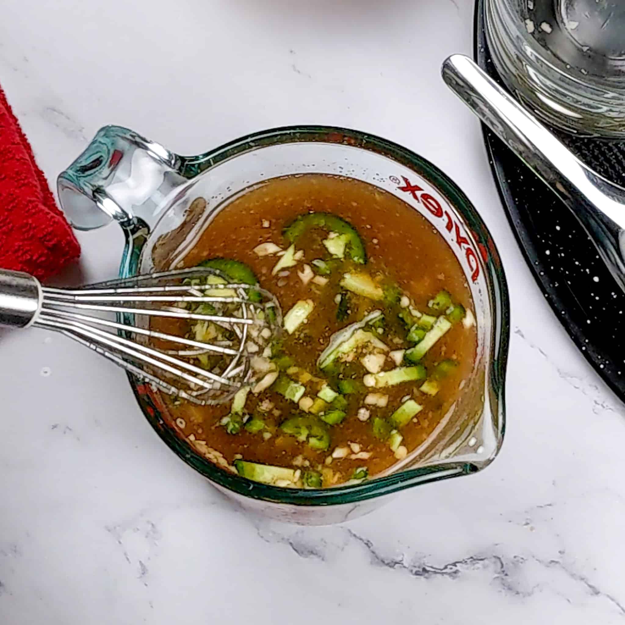 the Spicy Honey Jalapeno Lime seasoned chicken broth in a measuring cup with a whisk