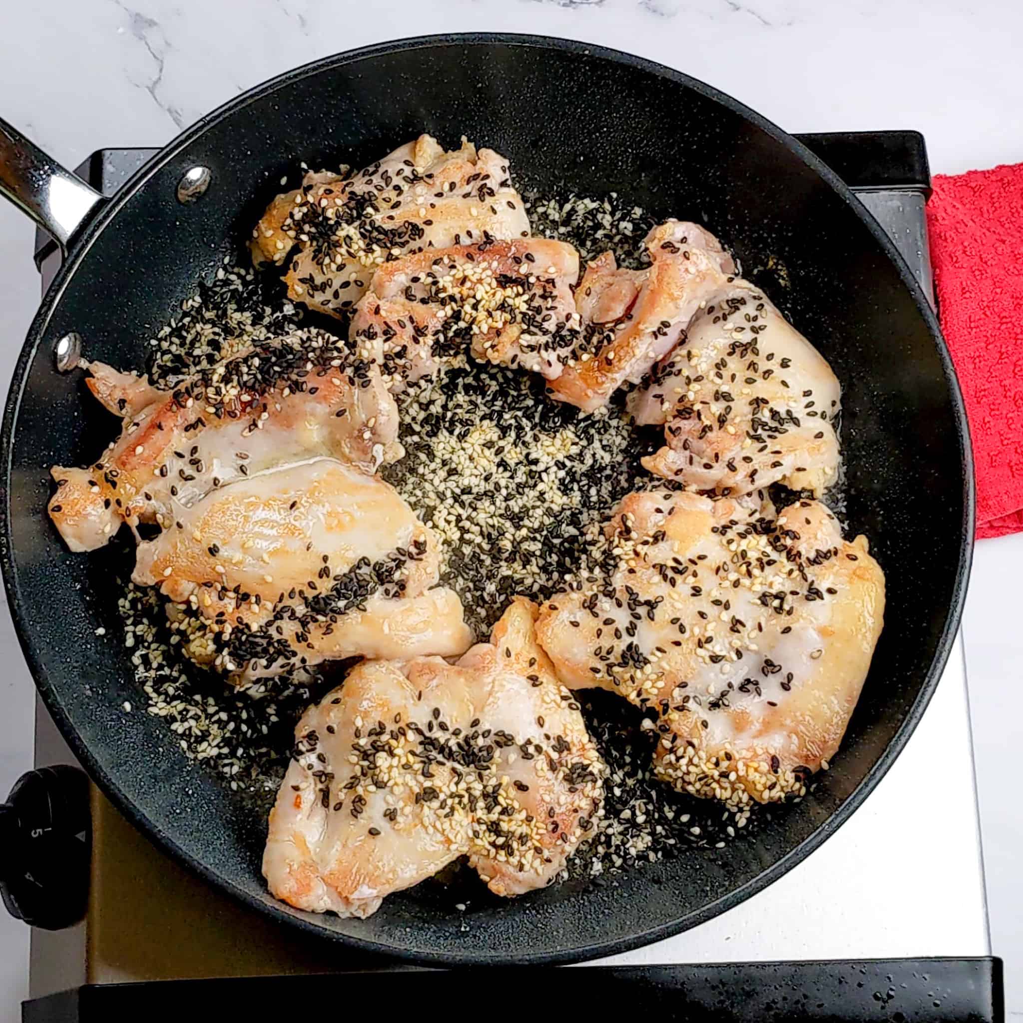 seared chicken breast with black and white sesame seeds in a non-stick frying pan