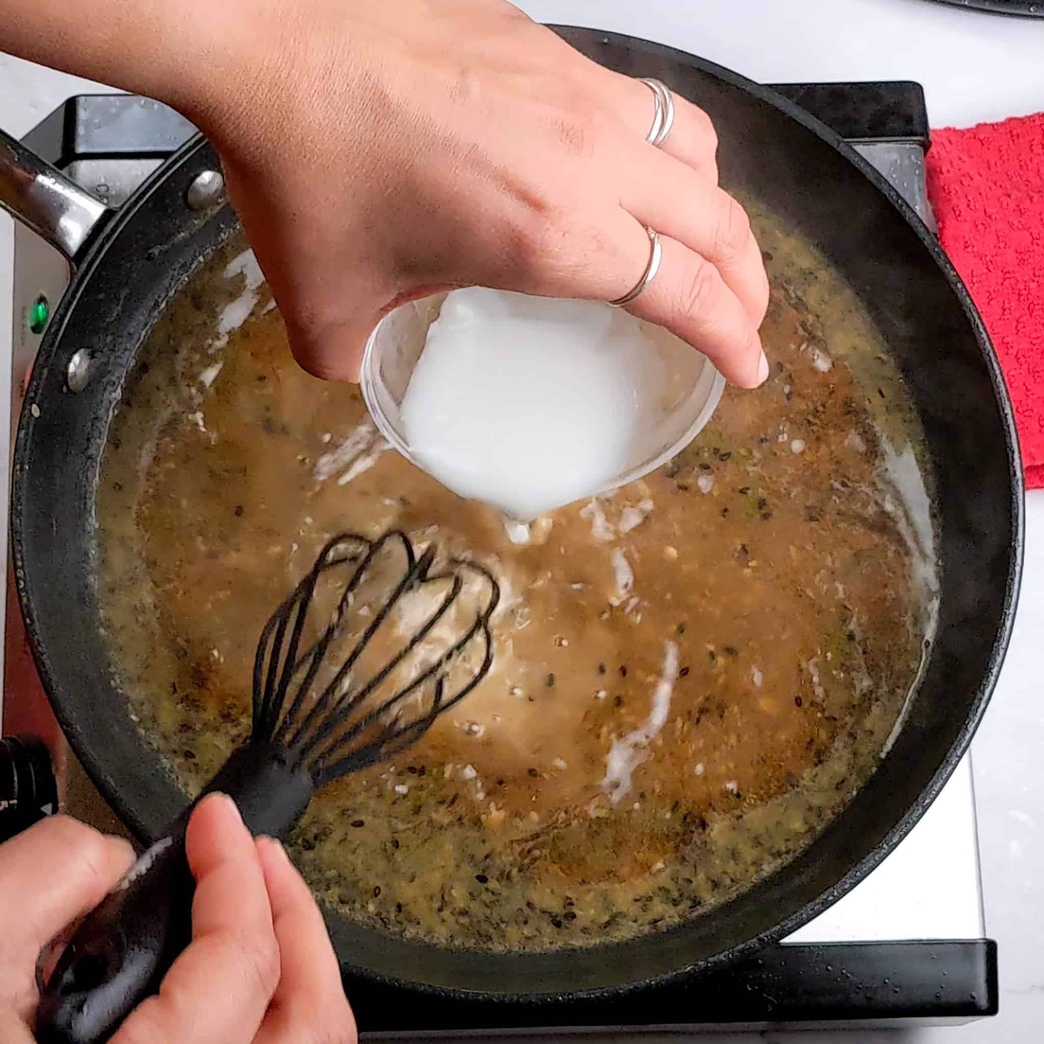 cornstarch slurry in a glass small bowl is being poured into the Spicy Honey Jalapeno Lime reduced sauce and being whisk together with a silicone whisk in a non-stick frying pan.