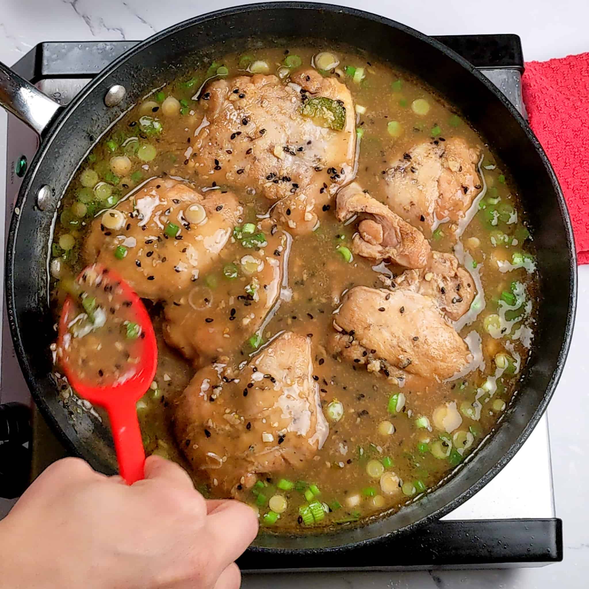 a silicone spoon pour the reduced finished Spicy Honey Jalapeno Lime sauce over the chicken thighs coated in sesame seeds and sliced scallions in a non-stick frying pan