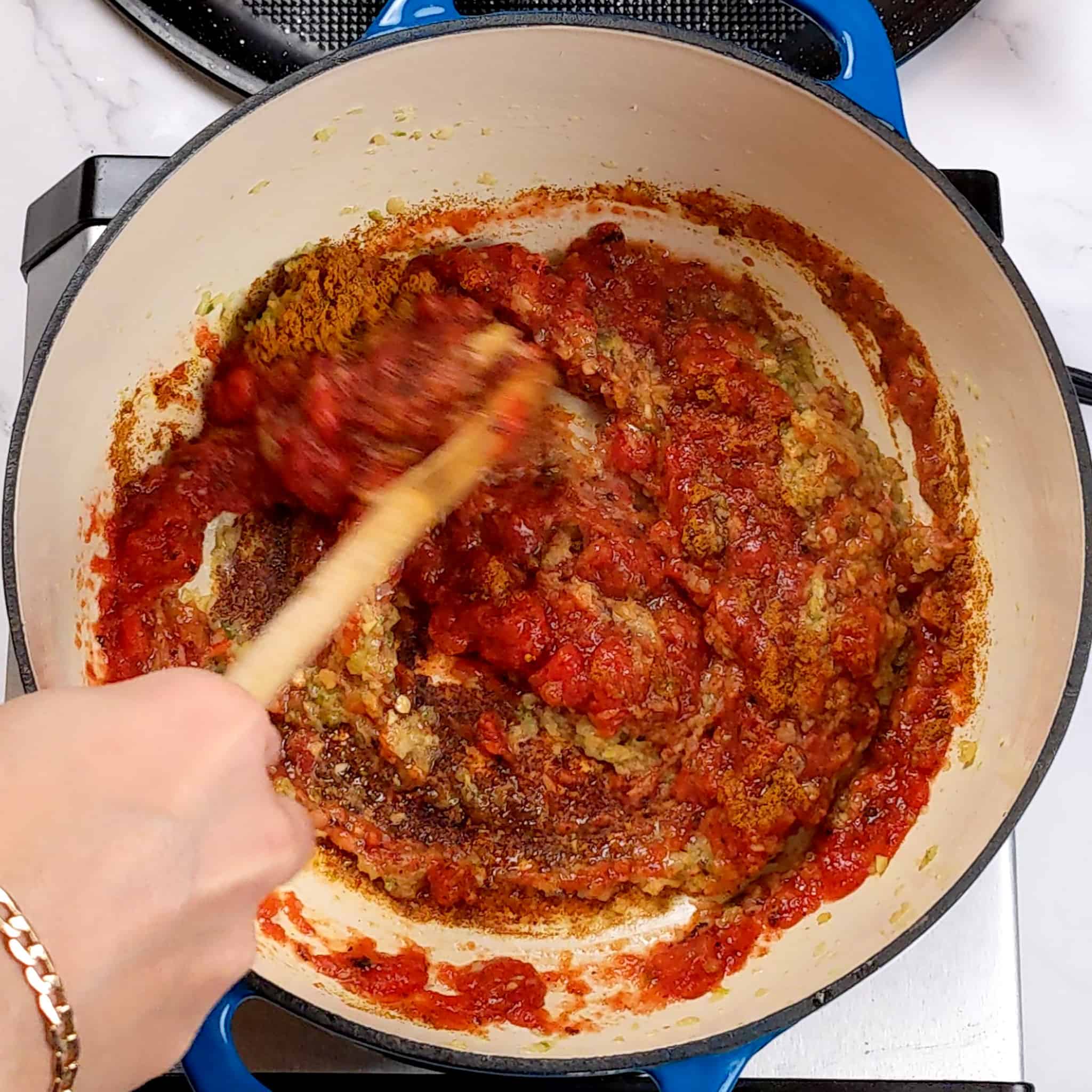 the tomato based paste sauce for the bean kale tomato stew recipe in a dutch oven being mixed with a wooden spoon