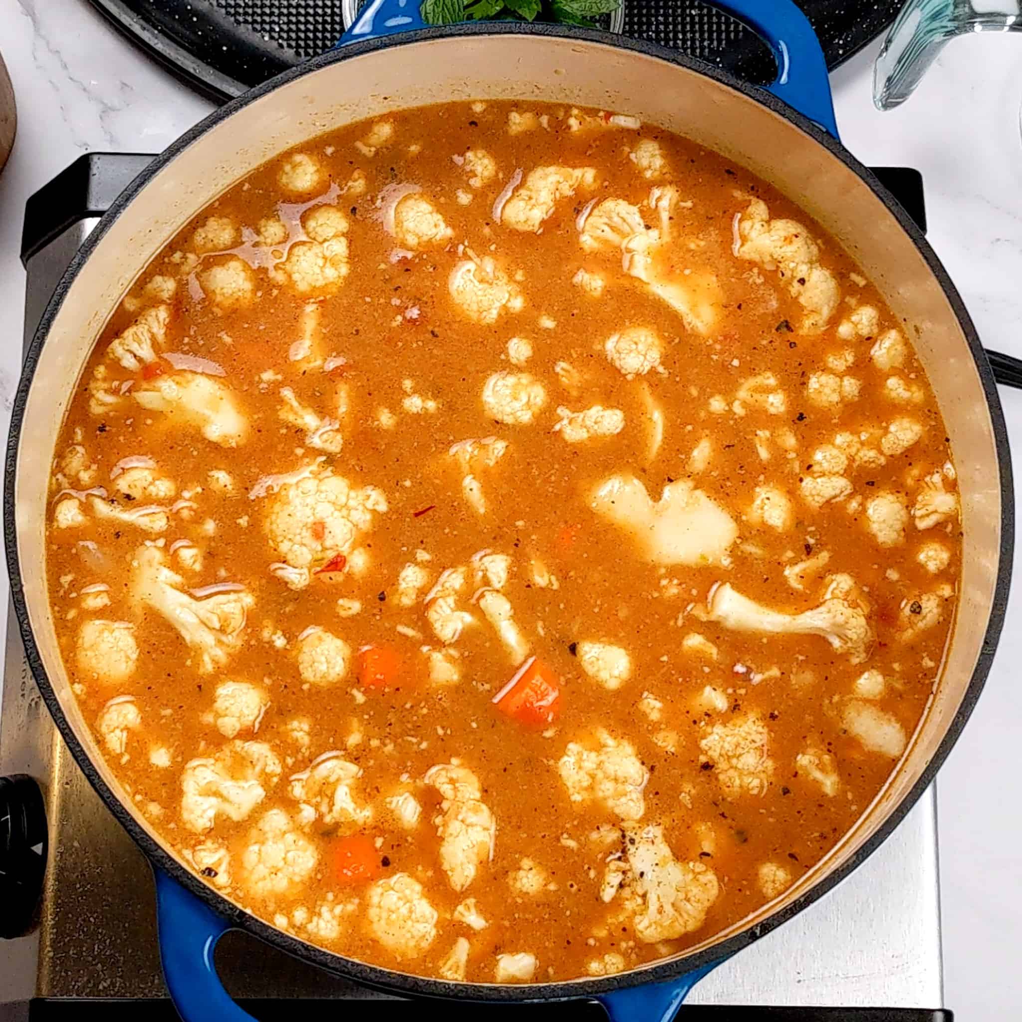 tomato base broth with floating cauliflower florets in a dutch oven