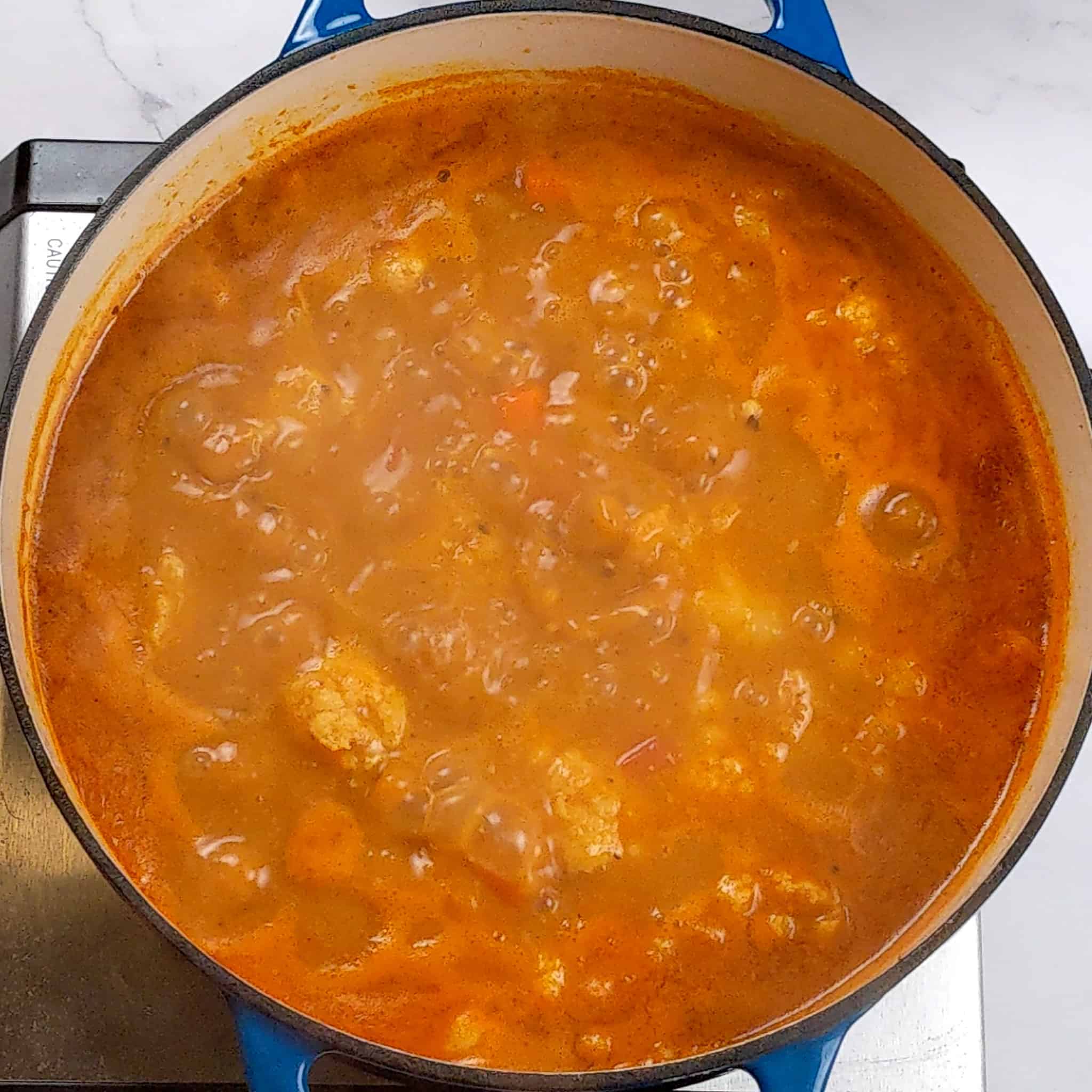 thick tomato base coconut broth simmering in a dutch oven