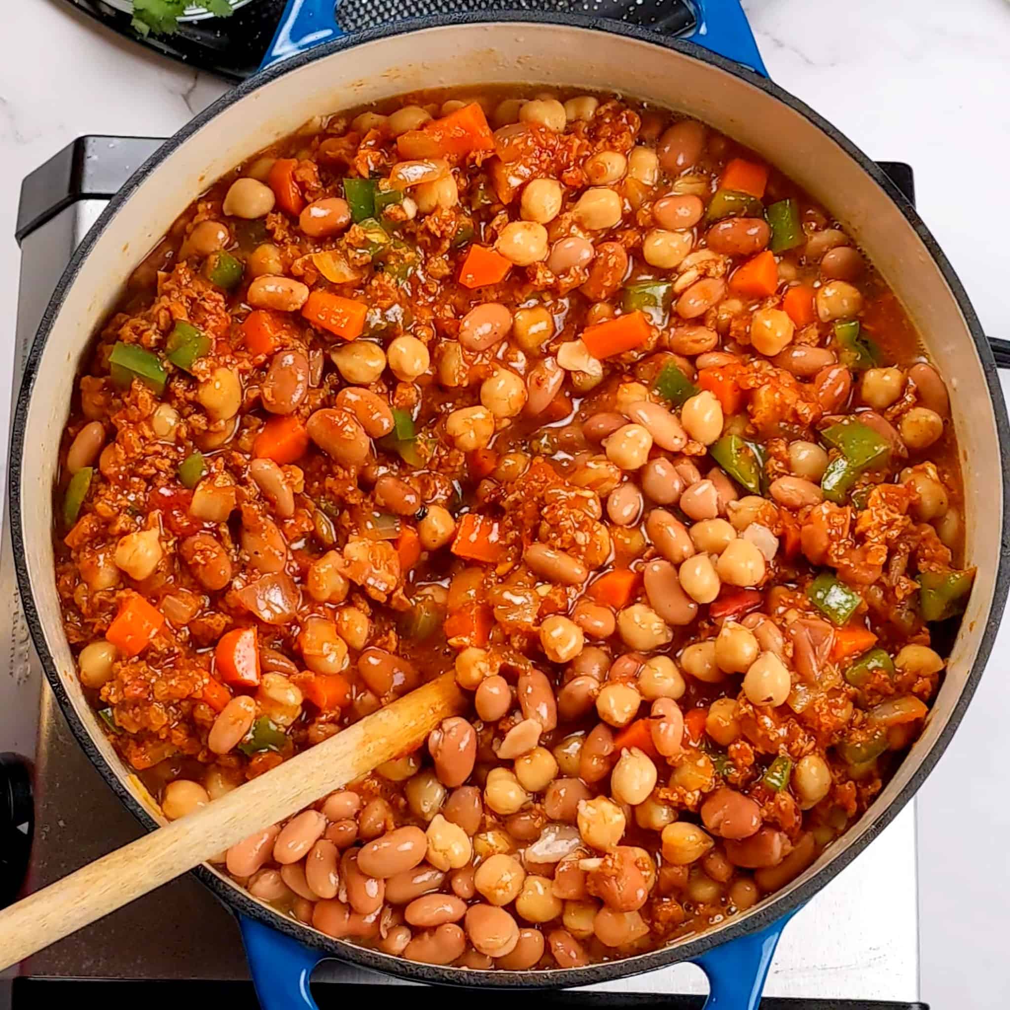 chickpeas and cannellini beans added to the crumbled soy chorizo and diced vegetables mixture with a wooden spoon in a a dutch oven