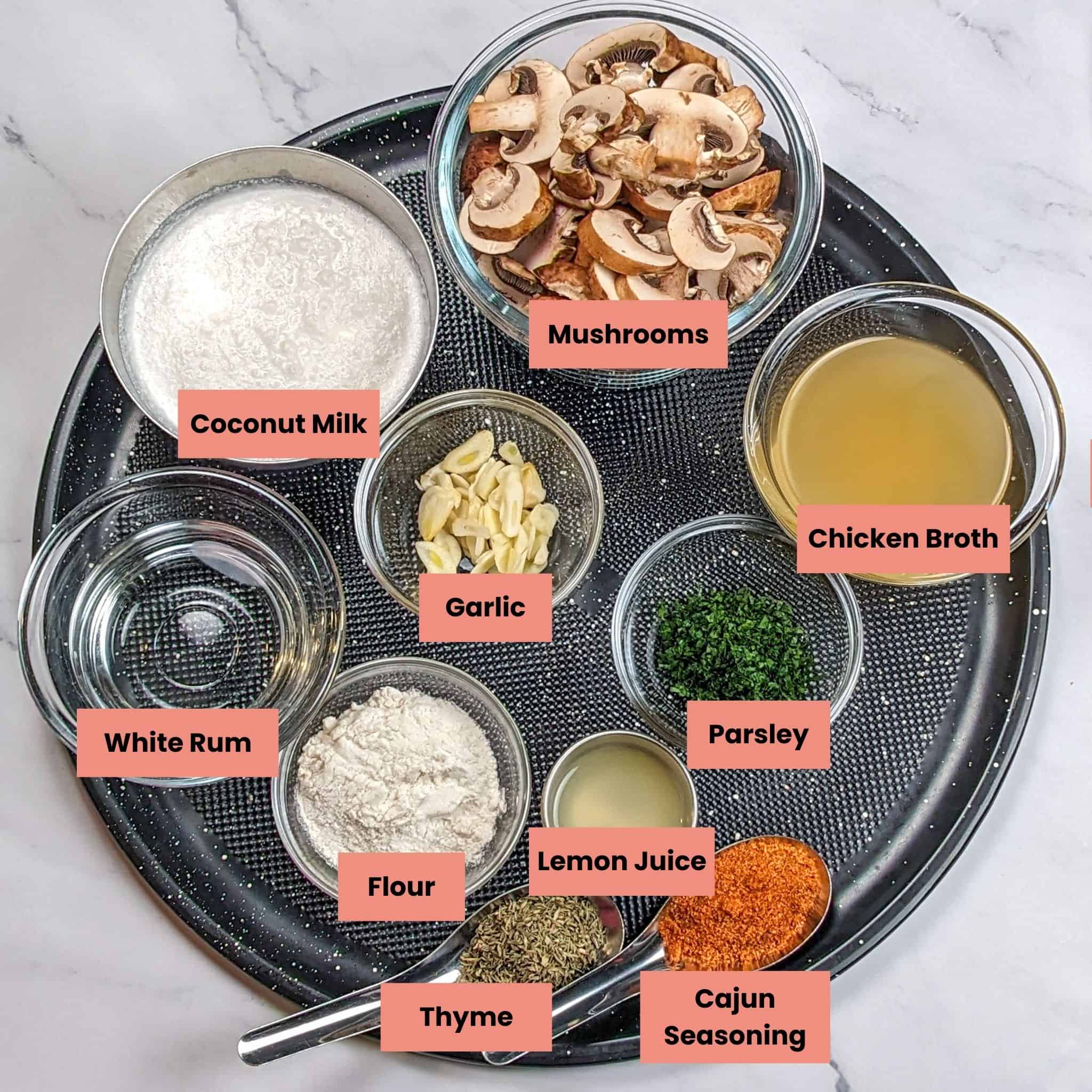 labeled ingredients for the Easy Spicy Creamy Coconut Mushroom Chicken with Rum recipe in containers on a large round pizza pan