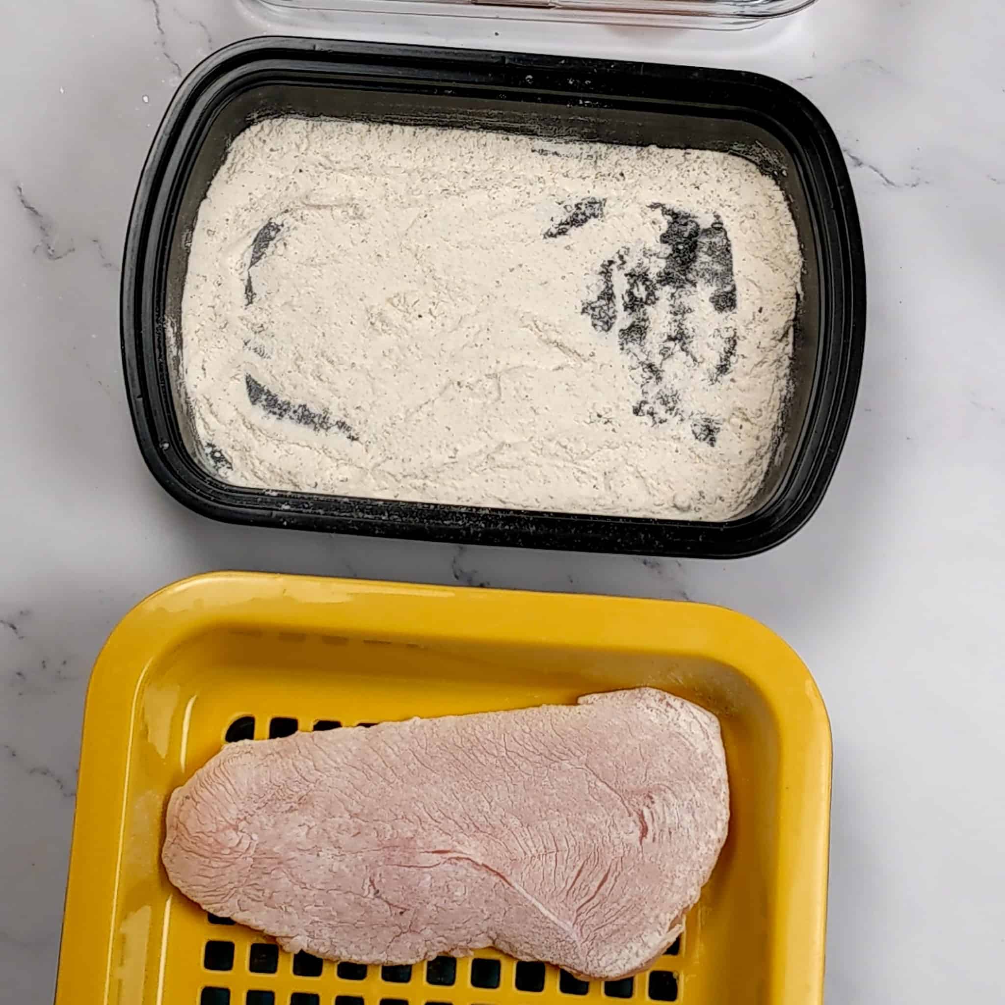 butterflied chicken breast dredge in seasoned flour resting on a plastic meat resting tray
