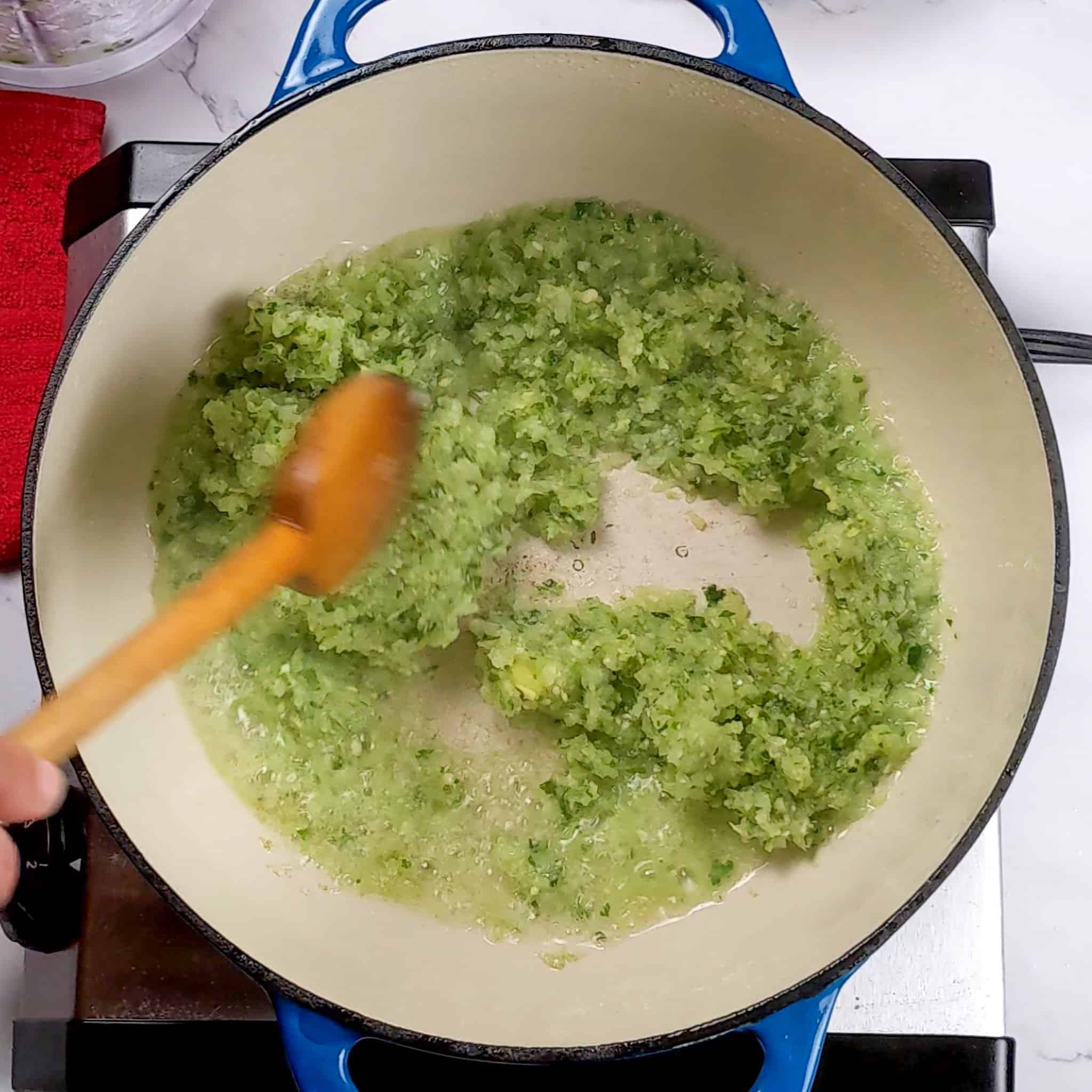 aromatic paste of garlic, ginger, onions, jalapeno and cilantro cooking down in a Lodge enameled dutch oven being stirred with a wooden spoon