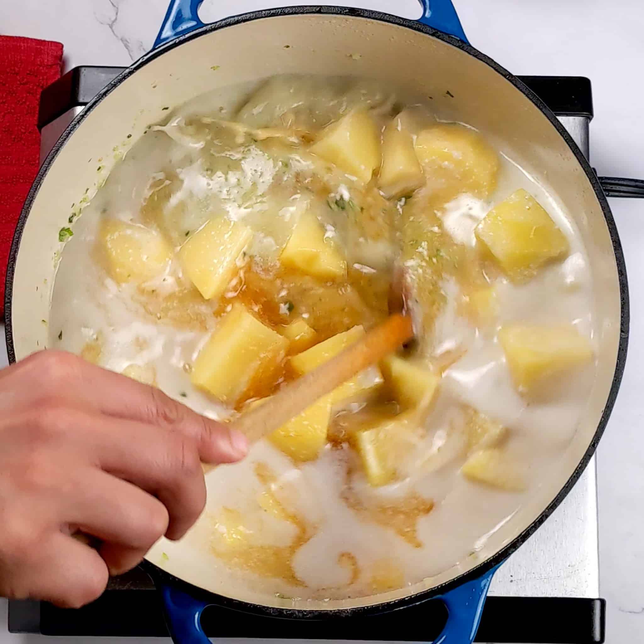 yukon gold potato chunks in a seasoned seafood coconut milk broth being stirred with a wooden spatula in a dutch oven