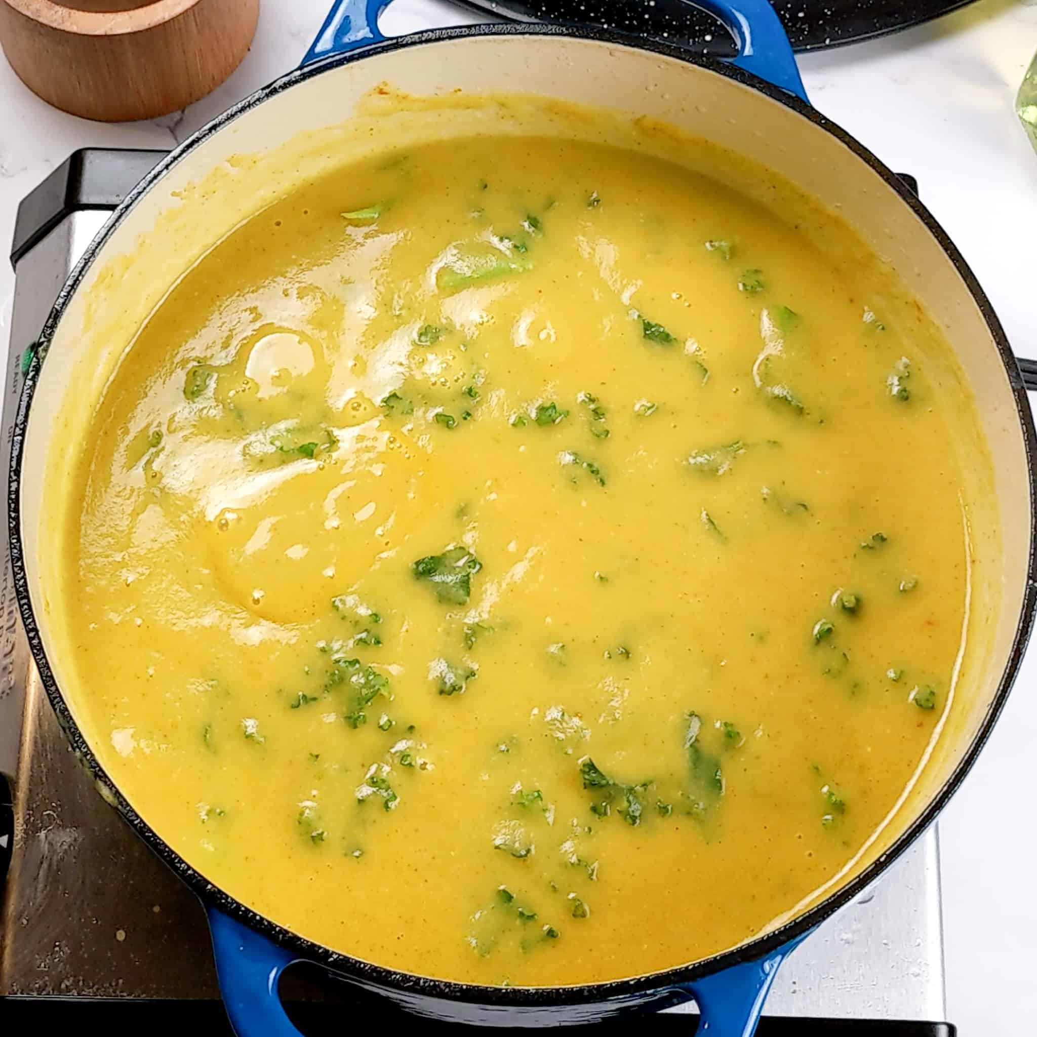 creamy curry coconut potato soup with shredded kale simmering in a dutch oven