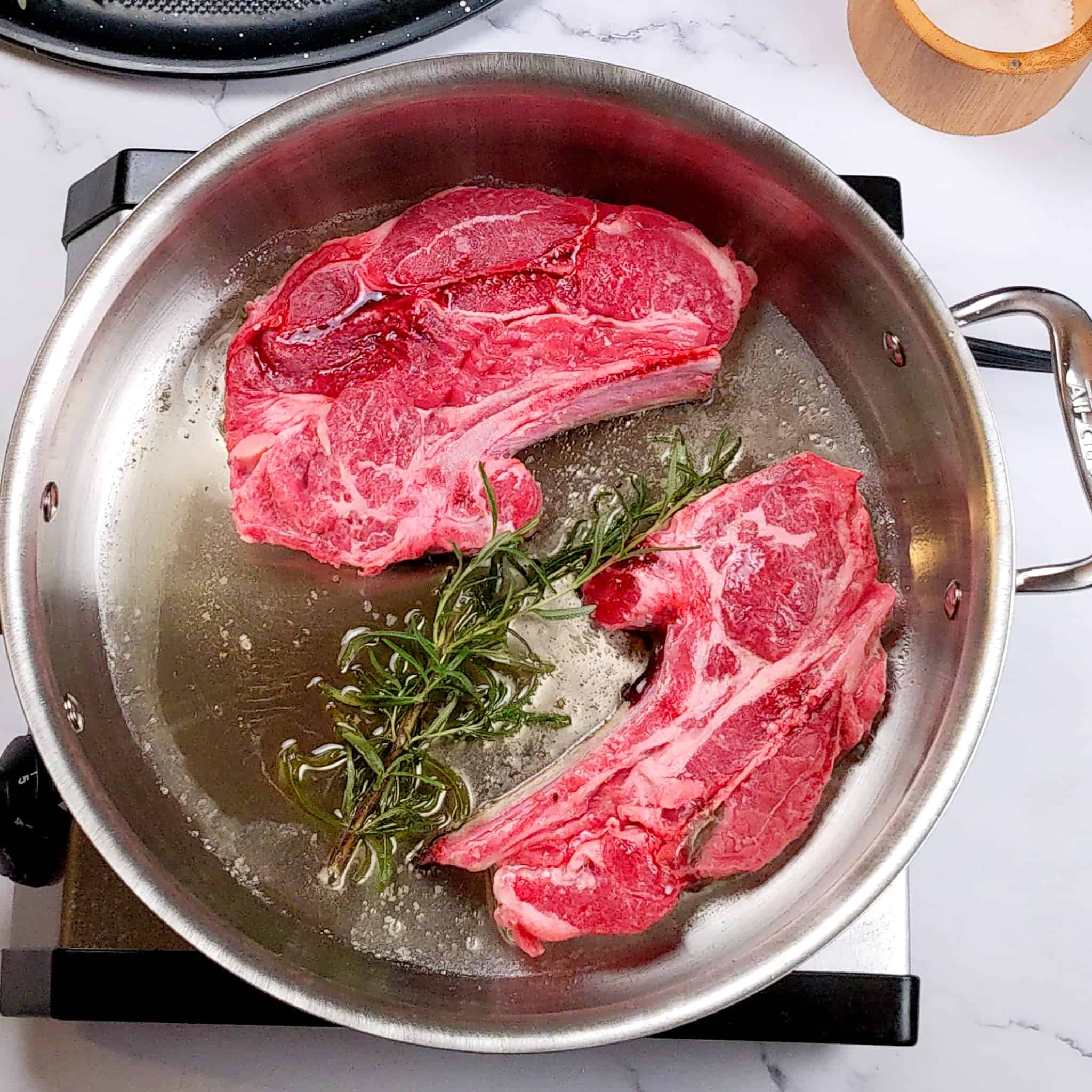 lamb shoulder chops with rosemary searing in an all-clad stainless steel sauté pan