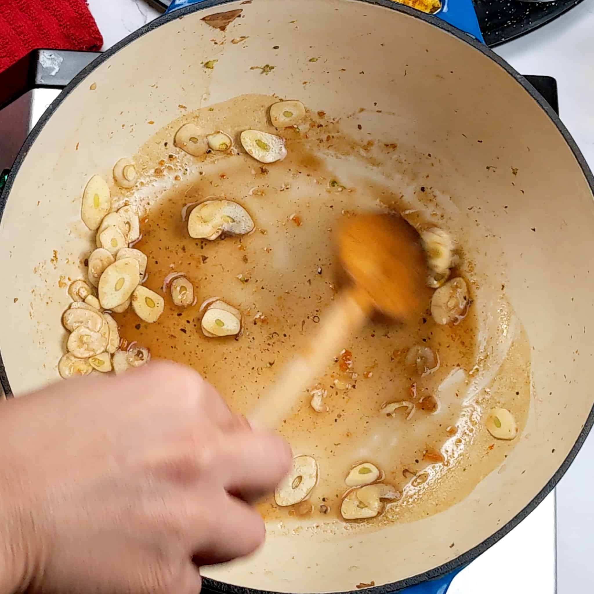 sliced garlic sauteing in a Dutch oven with a wooden spoon