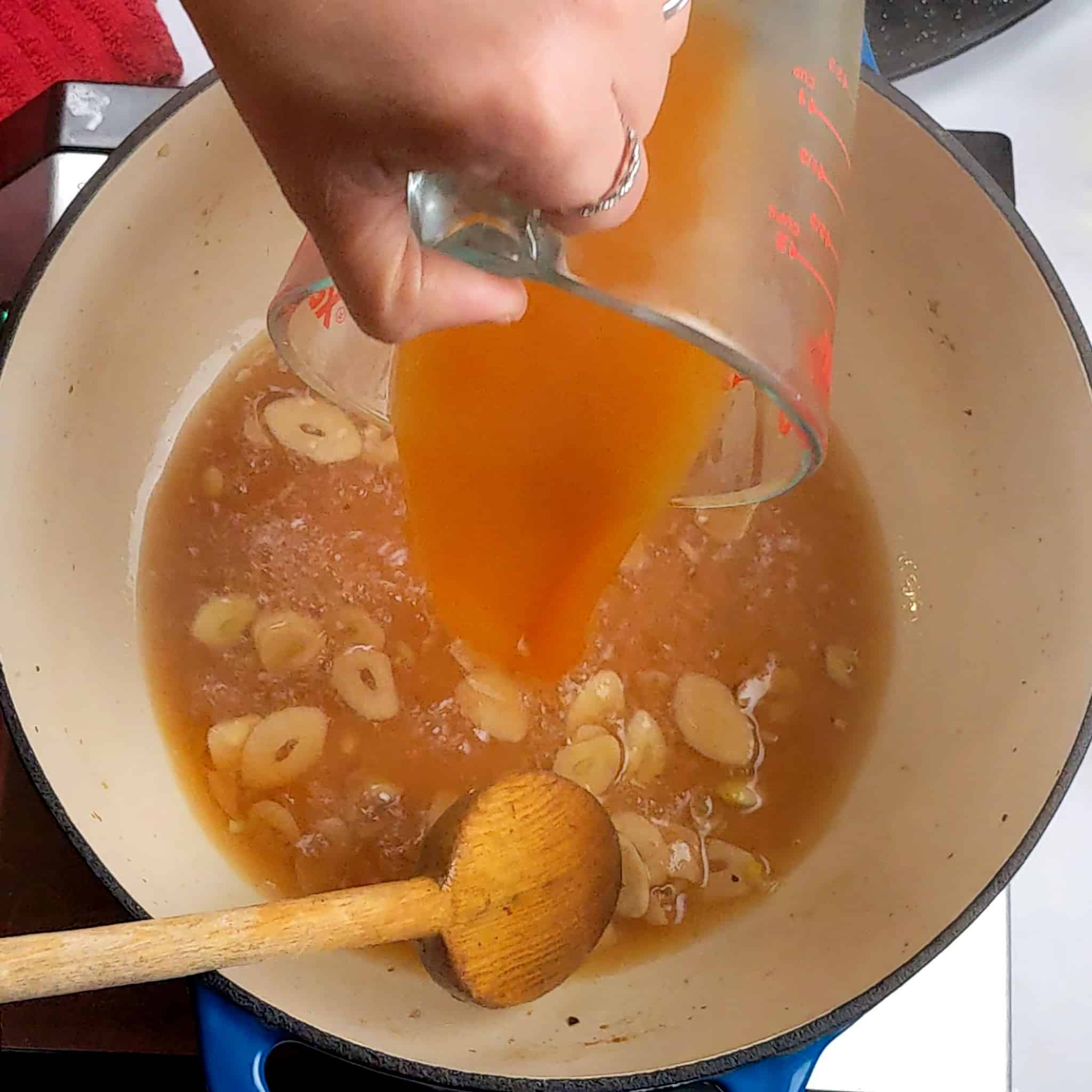 vegetable broth being poured into the wine soaked sliced garlic in the dutch oven