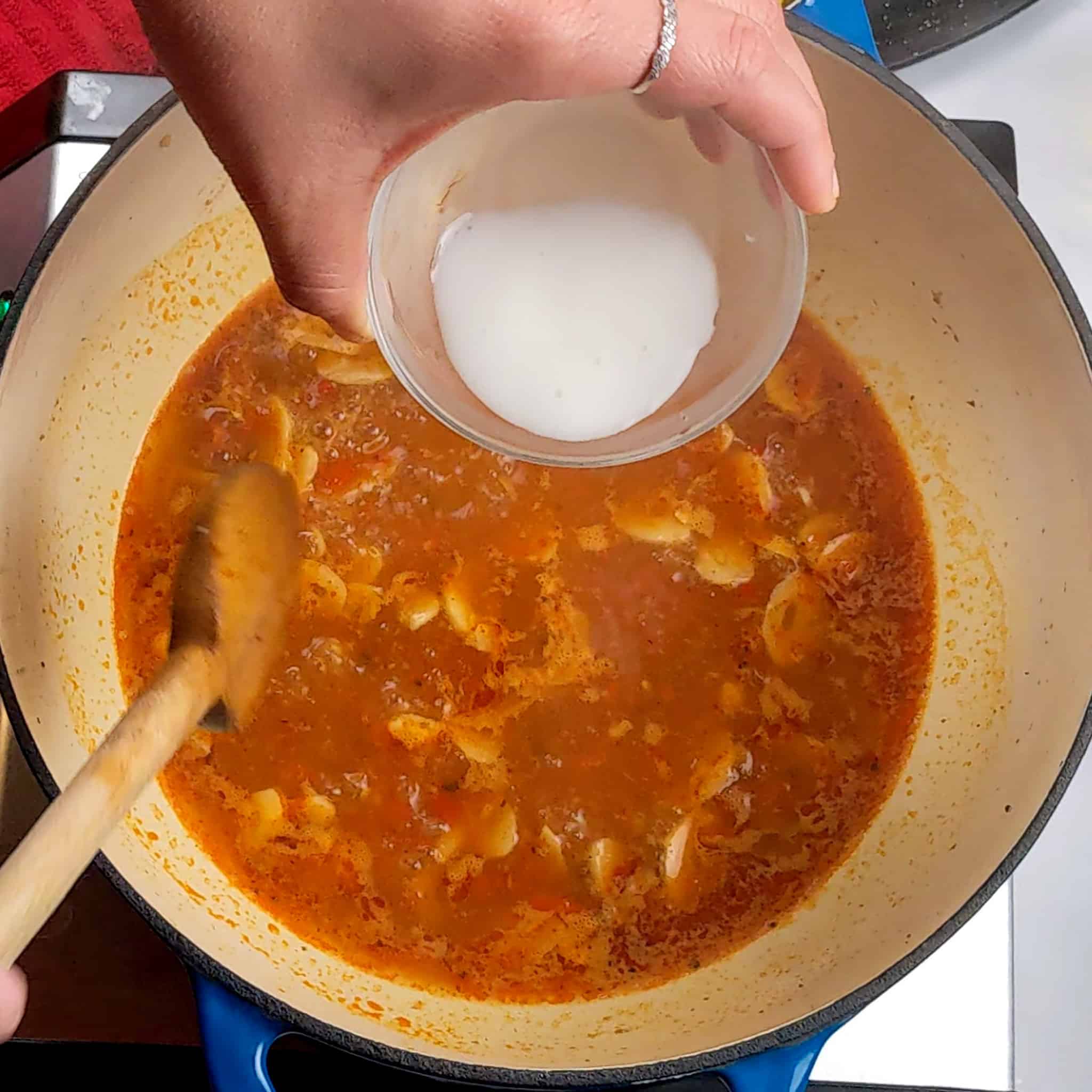 cornstarch slurry being added to the simmering sauce in the dutch oven for the chili lemon garlic shrimp and vegetable recipe